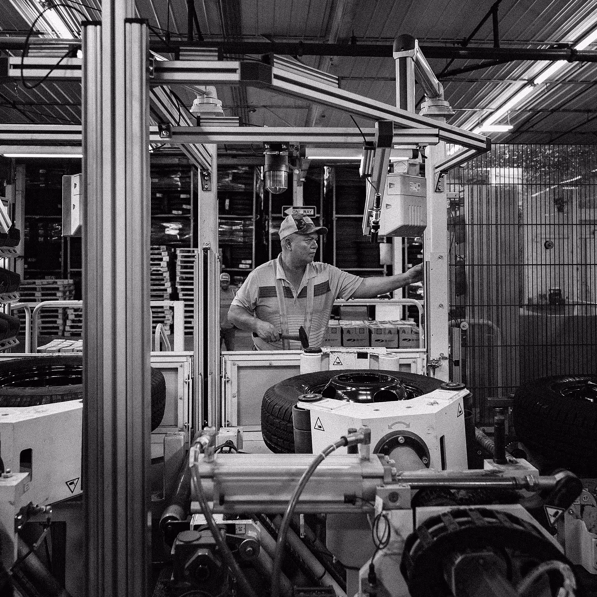 Man working on machinery inside a tire manufacturing facility with tires and industrial equipment around.