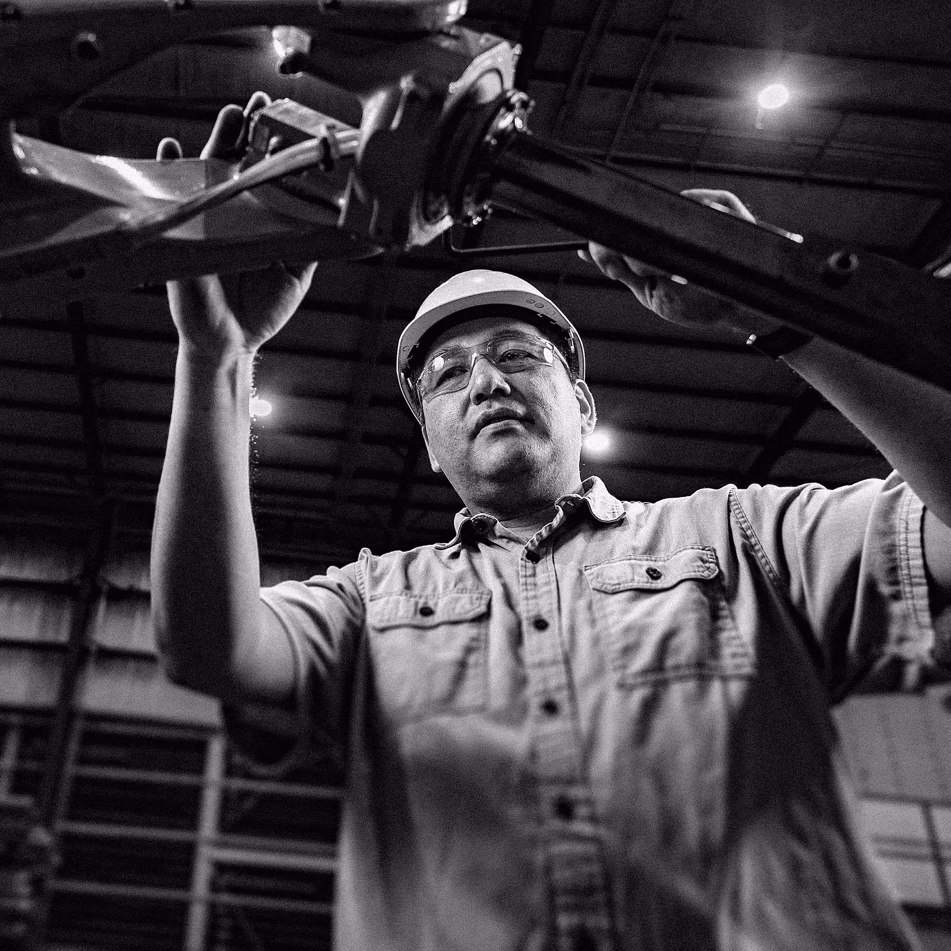 Worker wearing a hard hat and safety glasses inspecting mechanical equipment in an industrial facility.