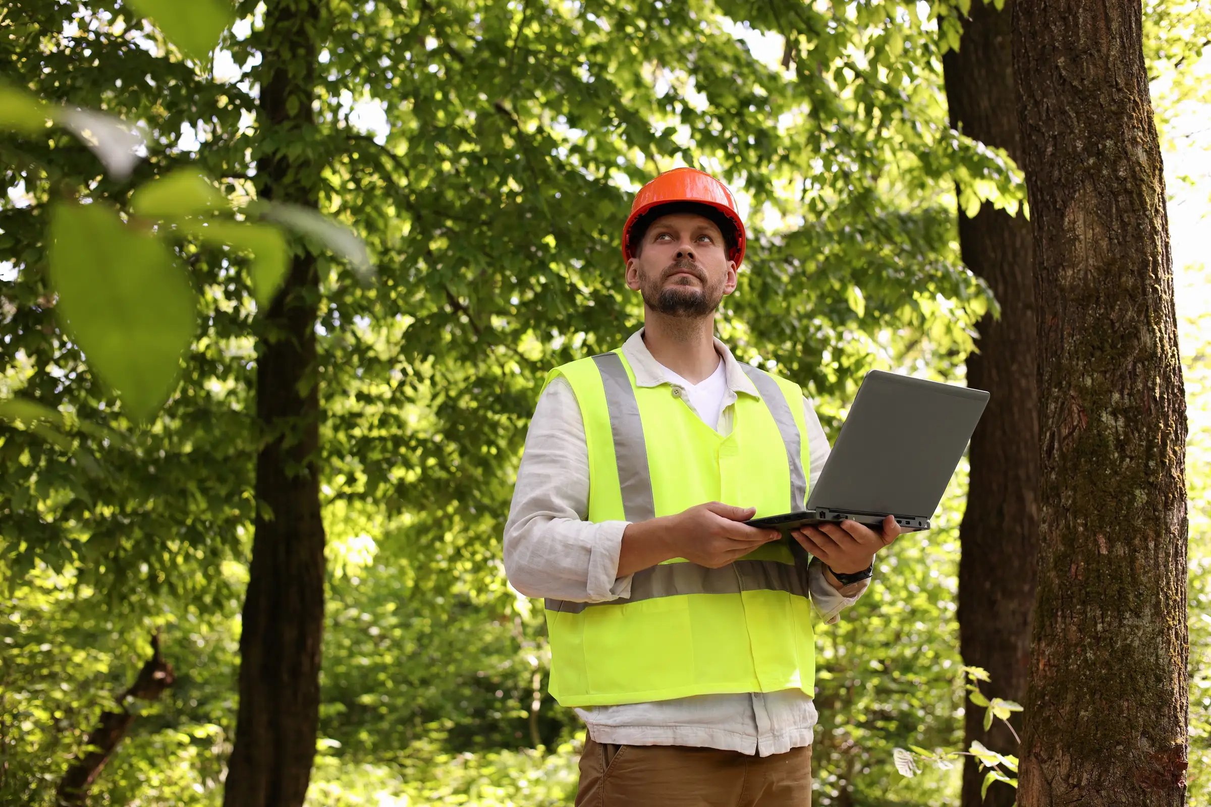 Man wearing construction uniform holding laptop in a forest