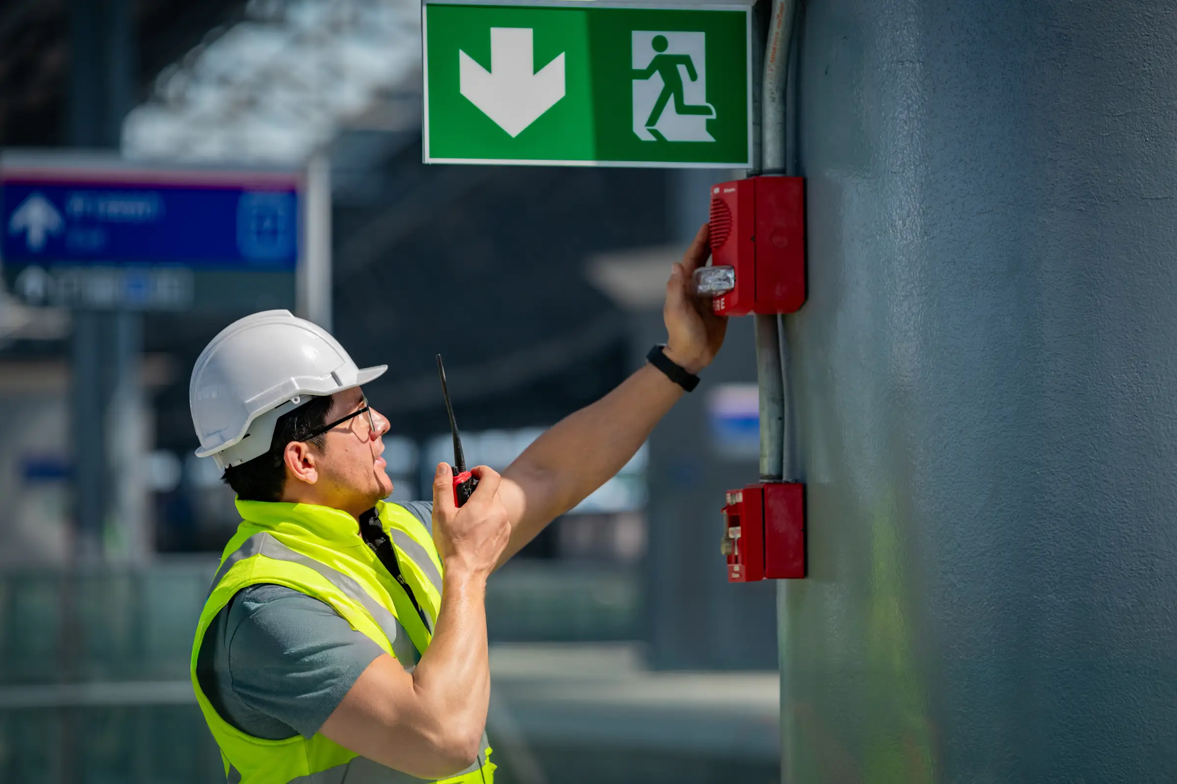 Man in construction uniform checking fire alarm under an exit evacuation sign