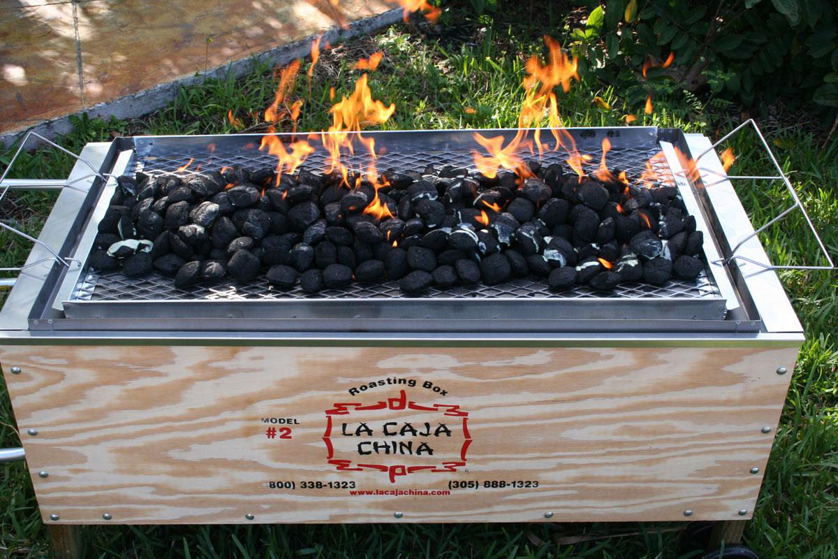Coals being lit on top of Caja China at backyard catering event