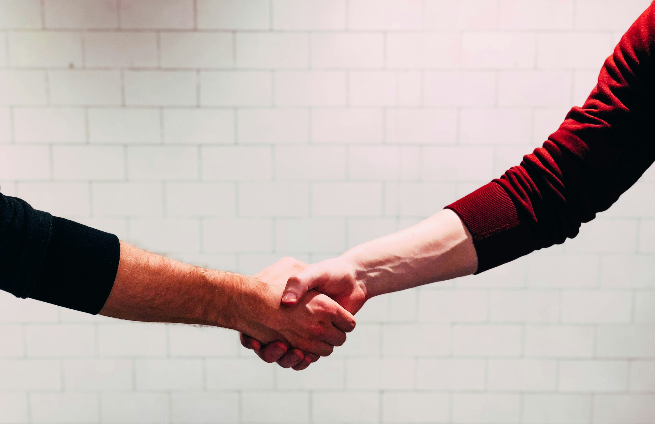 Two individuals shaking hands in front of a white tiled wall.