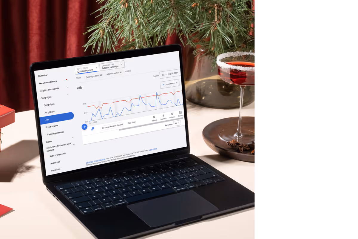 A sleek laptop displaying an analytics dashboard on a table set for a festive occasion, including a cocktail and holiday decorations in the background.