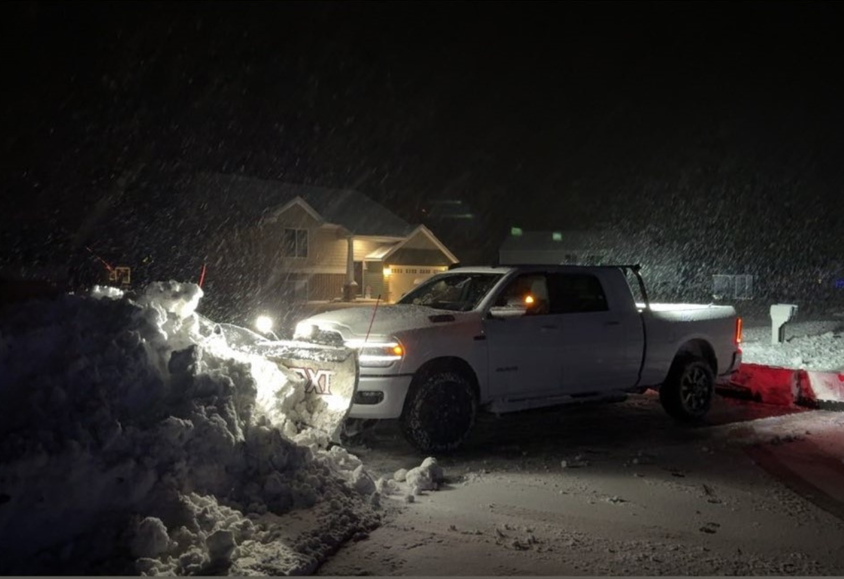 White pickup truck with snow plow clearing snow on a driveway at night during heavy snowfall.