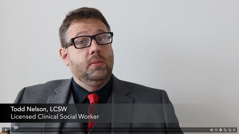 Man with glasses, beard, and mustache wearing a gray suit, black shirt, and red tie against a plain background with text identifying him as Todd Nelson, LCSW, Licensed Clinical Social Worker.