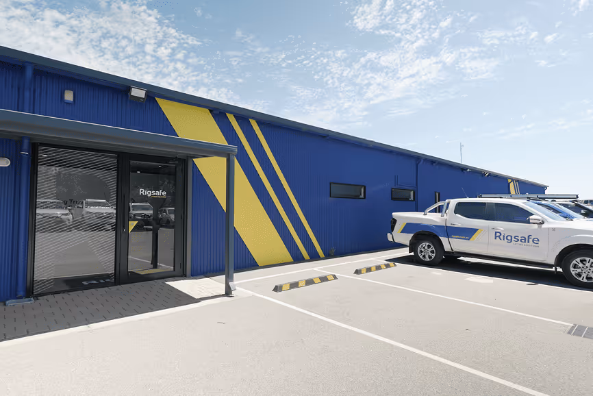 Exterior view of a blue building with yellow diagonal stripes and a Rigsafe-branded white pickup truck parked outside.