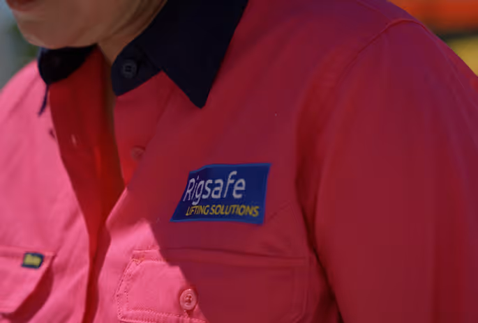 Close-up of a person wearing a red shirt with a blue and yellow Rigsafe Lifting Solutions logo patch.