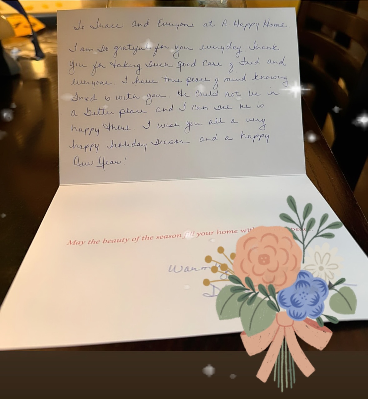 Open greeting card with handwritten message thanking staff at A. Happy Home for care of Fred, with printed floral decoration and seasonal wishes.