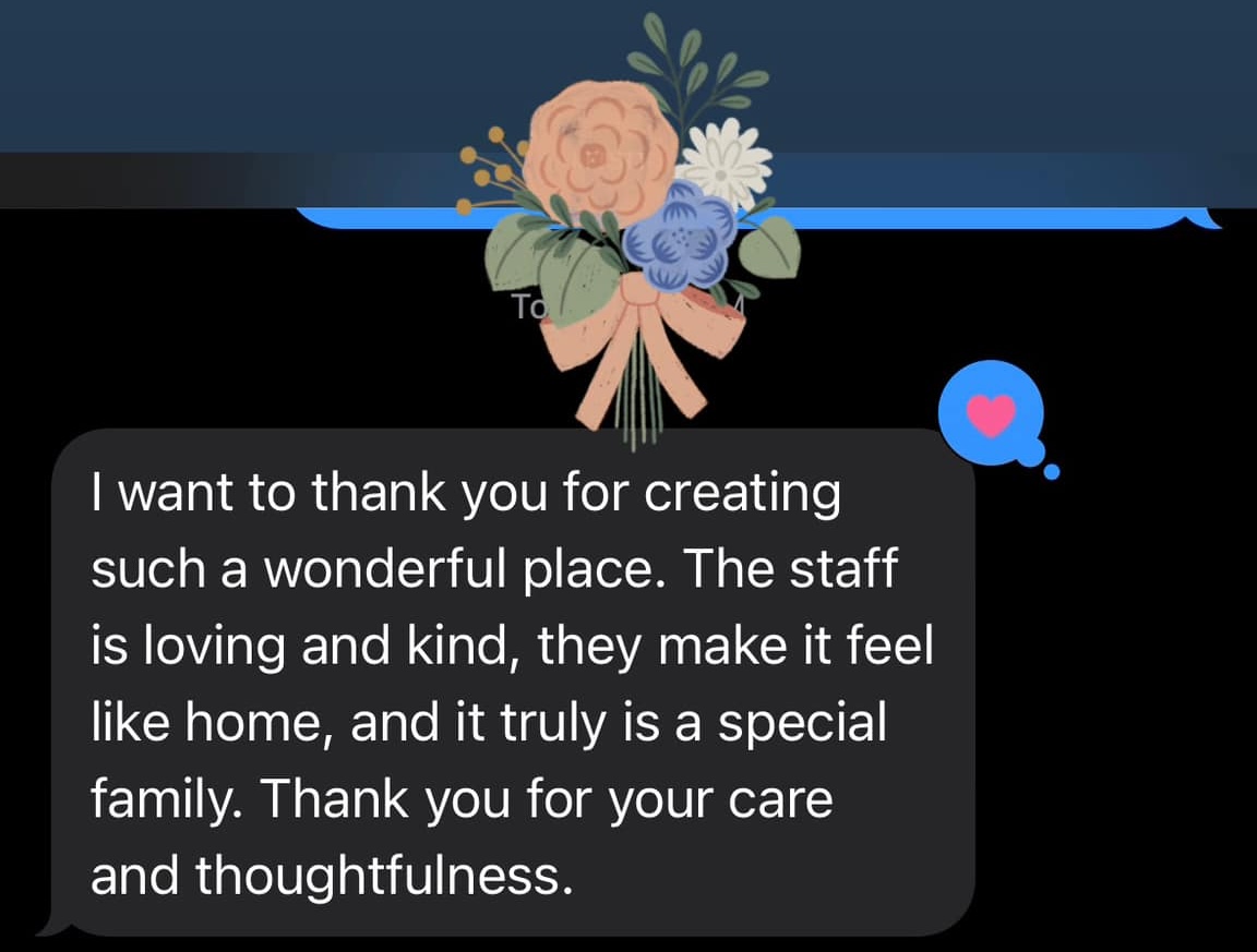 Text message expressing gratitude for a loving and kind staff that makes the place feel like home and a special family, thanking for care and thoughtfulness, with a floral decoration above the message and a heart reaction.