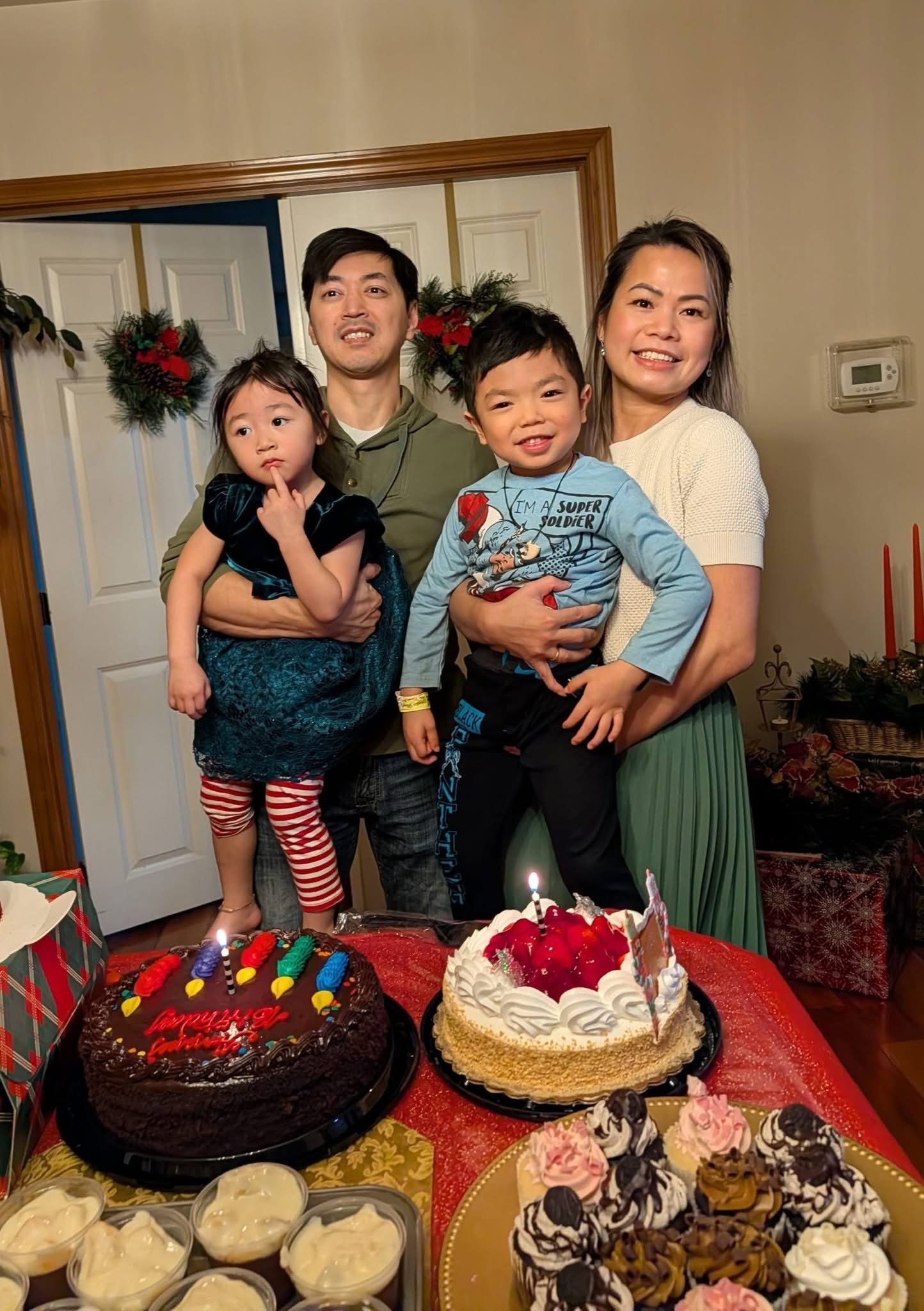A family of four with two children standing behind a table with two birthday cakes and assorted desserts.