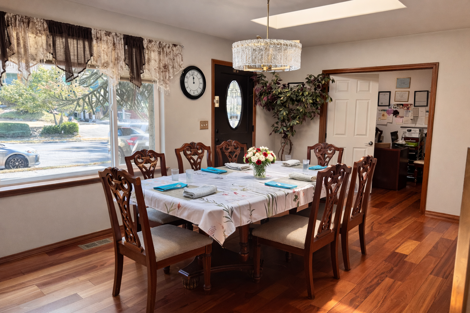 Dining room with a wooden table set for six, a floral centerpiece, and a chandelier overhead.