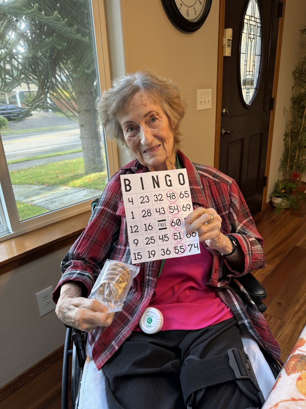 Elderly woman sitting in a wheelchair holding a bingo card with circled numbers and a packaged cookie.