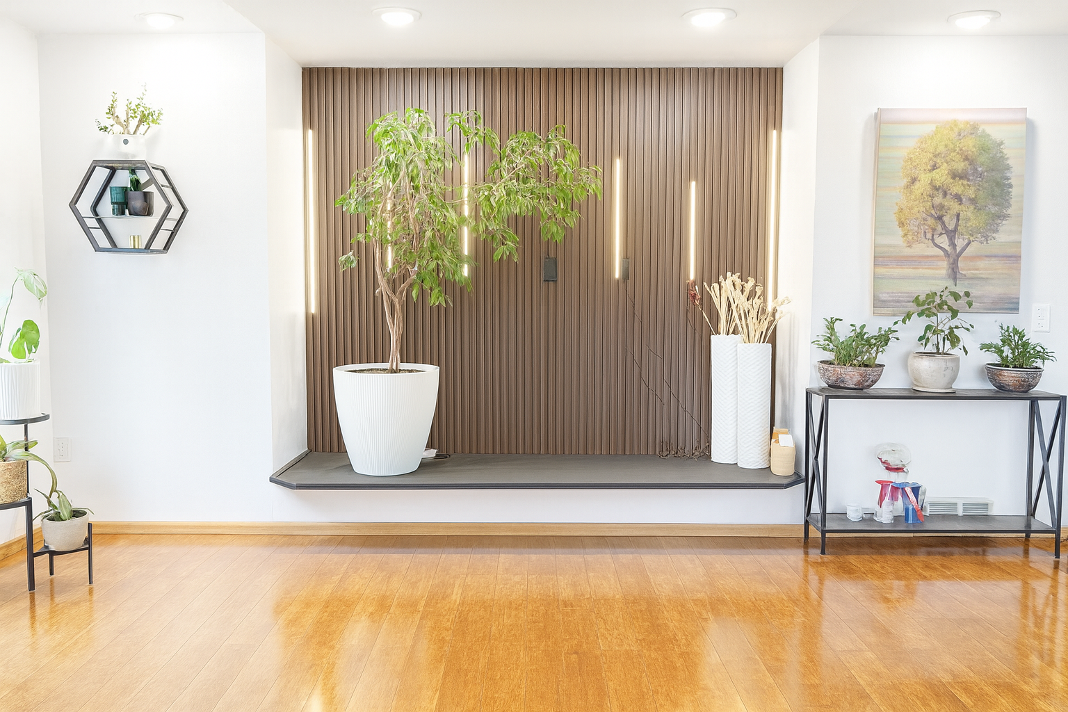 Bright modern living space with wooden floor, a large potted tree on a raised platform, decorative vases, and wall art featuring a tree.