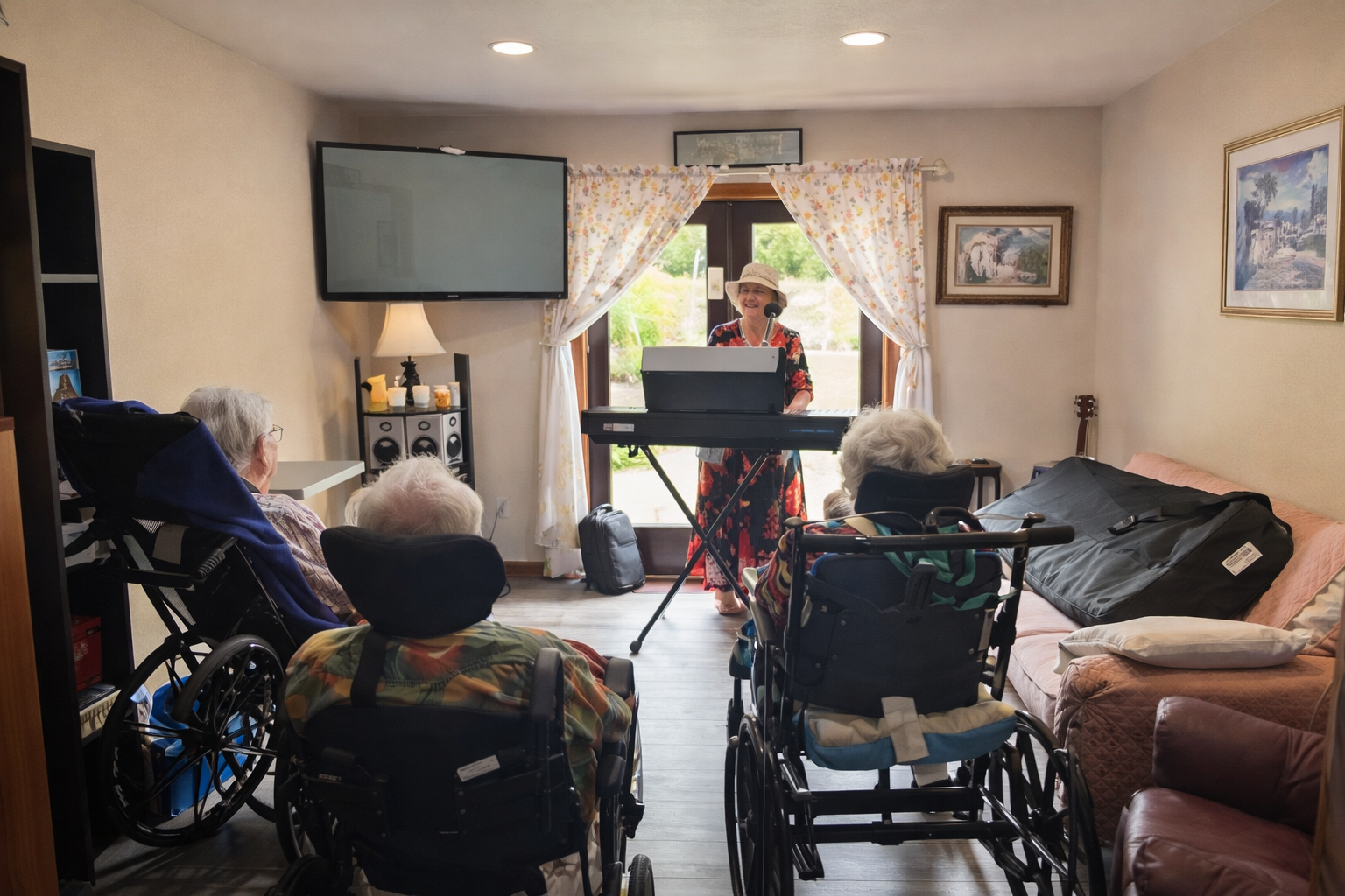 Woman in a floral dress and hat plays an electric piano for three elderly people in wheelchairs in a cozy living room.