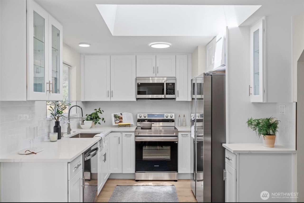 Bright modern kitchen with white cabinets, stainless steel appliances, a skylight, and wooden floor.