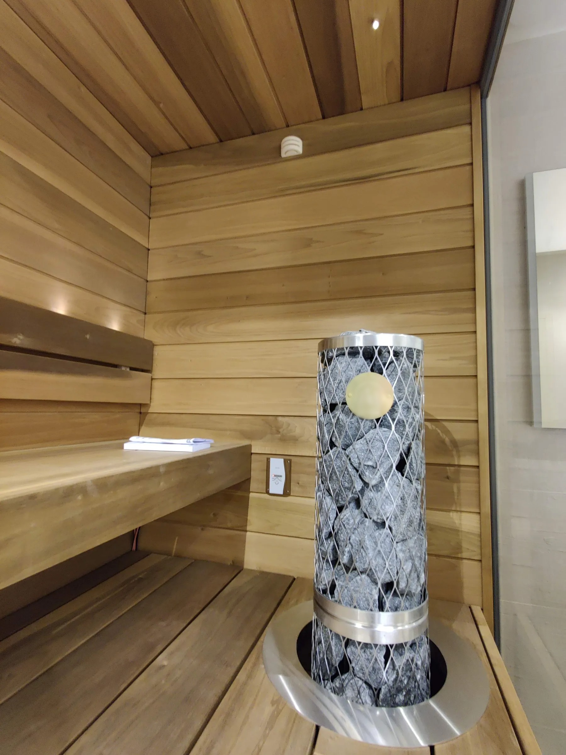 Puinen sauna, jossa on kivillä täytetty metallinen kiuas, puupenkit ja valkoinen pyyhe.