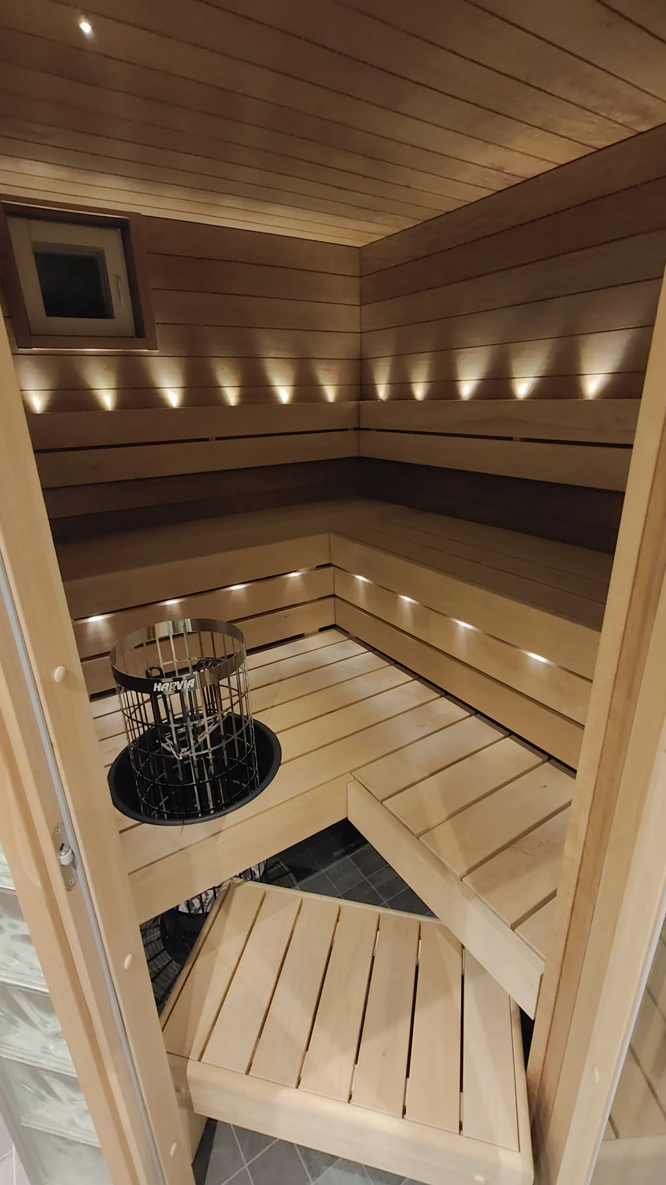 Sauna, jossa on puupanelointi, penkit ja kiuas, valaistus katossa ja seinissä.