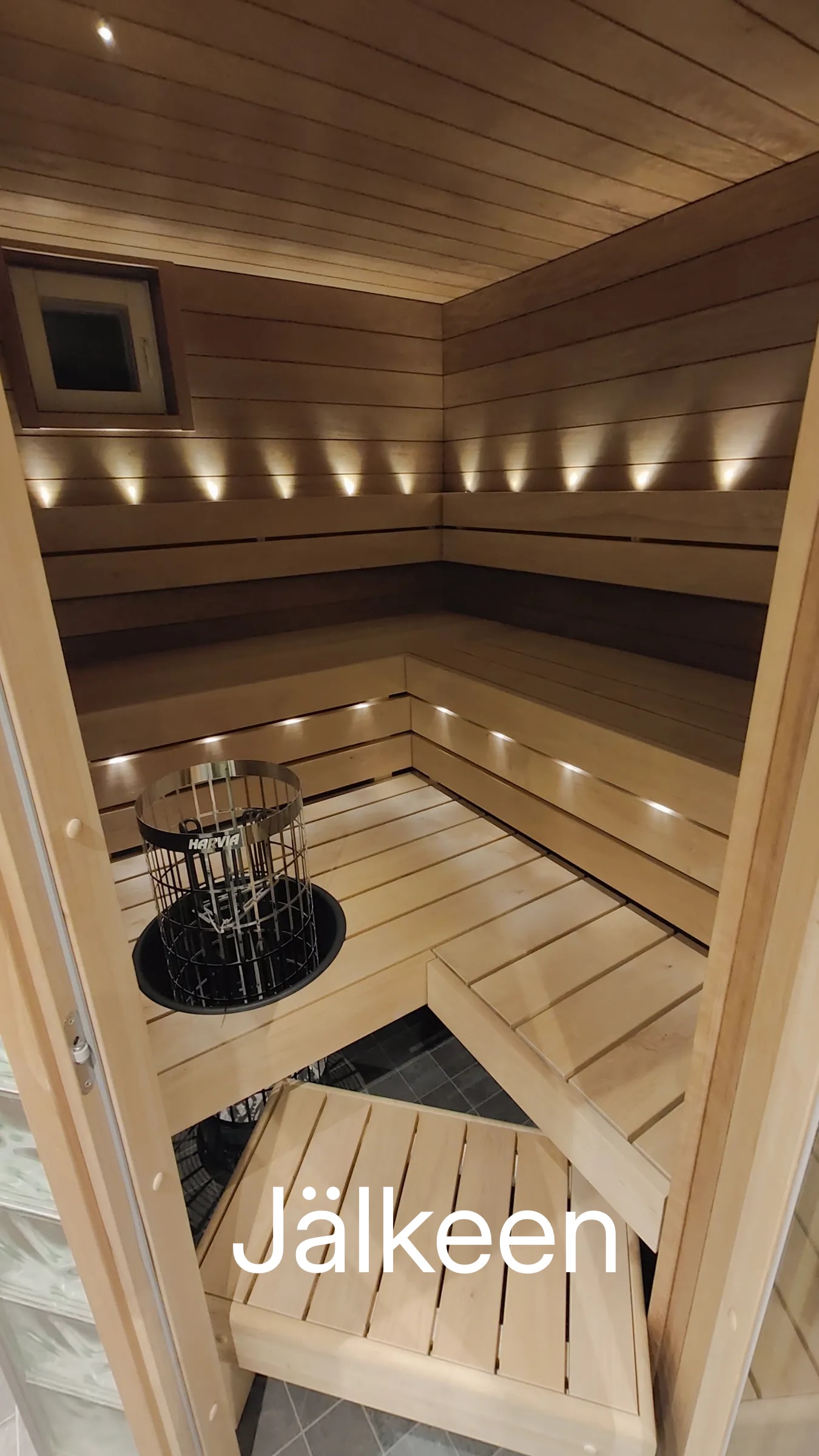 Sauna, jossa on puupanelointi, penkit ja kiuas. Valot luovat lämpimän tunnelman.