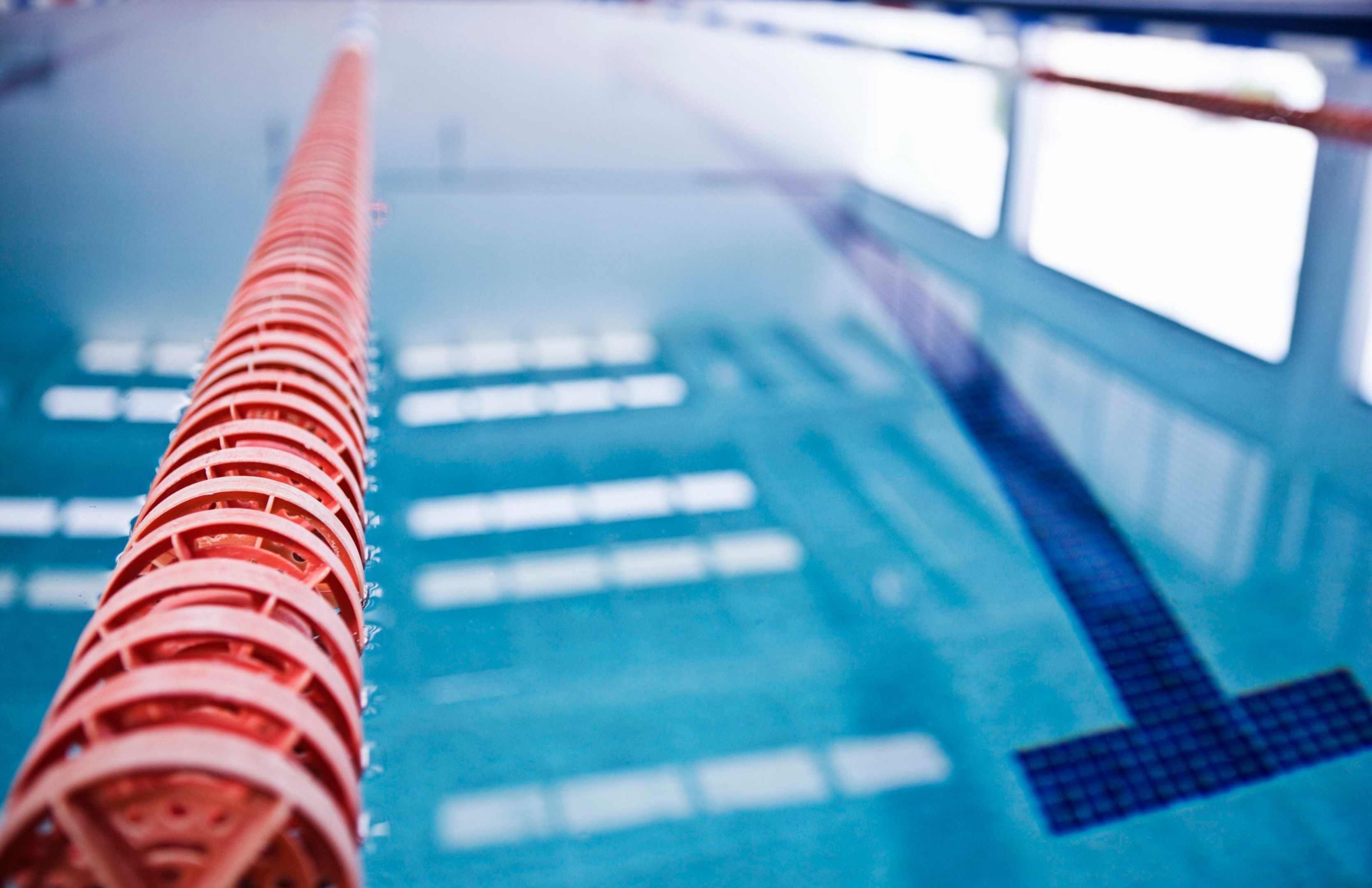 A bright red swimming lane rope features prominently, against the blurry blue background of a swimming pool.