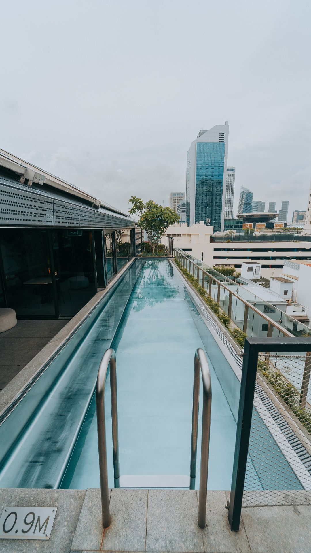 Top-down view of the rooftop lap pool at 21 Carpenter hotel, Singapore. The stainless steel handles of the pool ladder are right next to the depth marker, which indicates a pool depth of 0.9 metres.