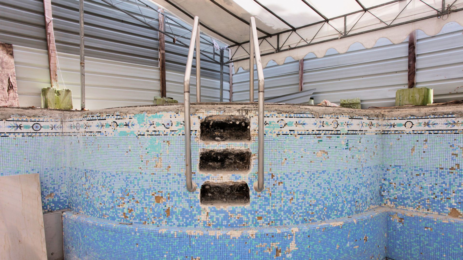The crumbling pool steps comprising blue and white tiles, and the rusty pool ladder of Ardmore Park condominium before renovation.