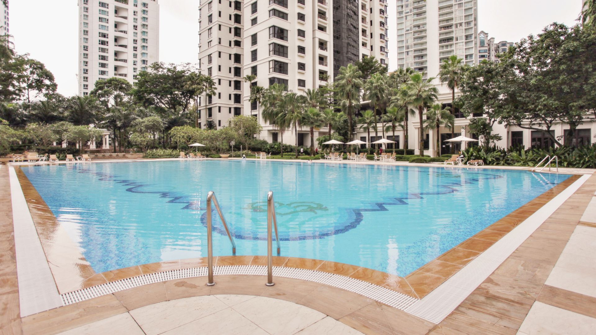 The curved edge of Ardmore Park swimming pool in Singapore at the deep end. A pair of stainless steel grab rails disappears down into the waters.