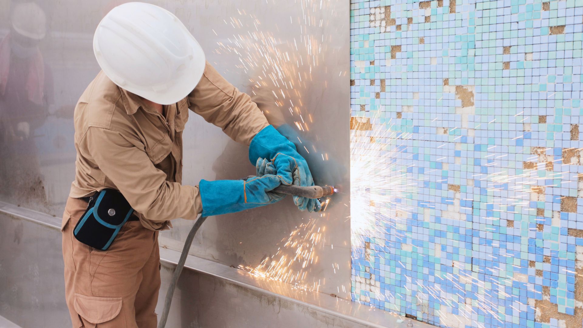 A worker wears a white helmet and protective gear, as he performs welding works for Ardmore Park's swimming pool upgrade. Bright sparks fly as he drills into the stainless steel sheet.