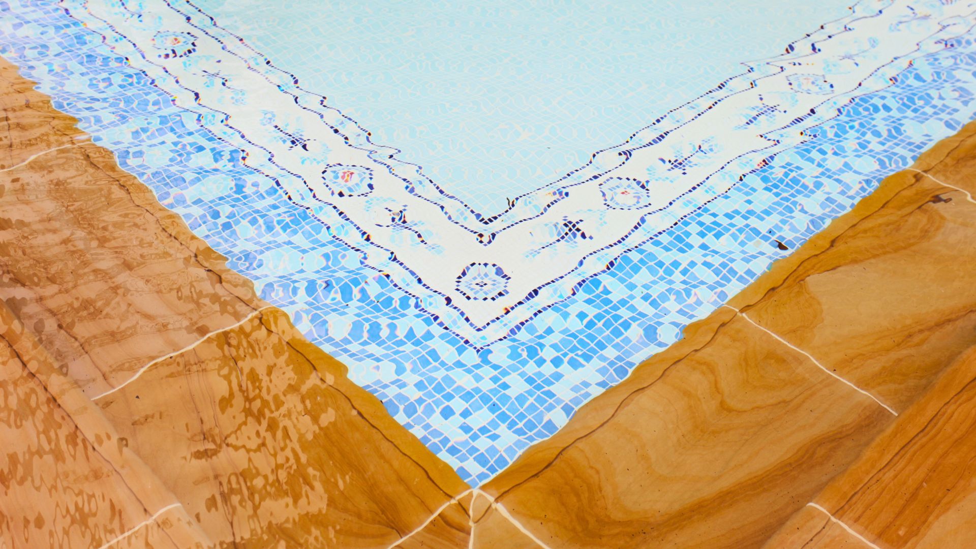 Close-up of the mosaic tiles decorating the border of Ardmore Park's swimming pool. The outer layer is made up of small blue and white tiles, whilst the inner section comprise larger tiles in a mediterranean-inspired pattern.