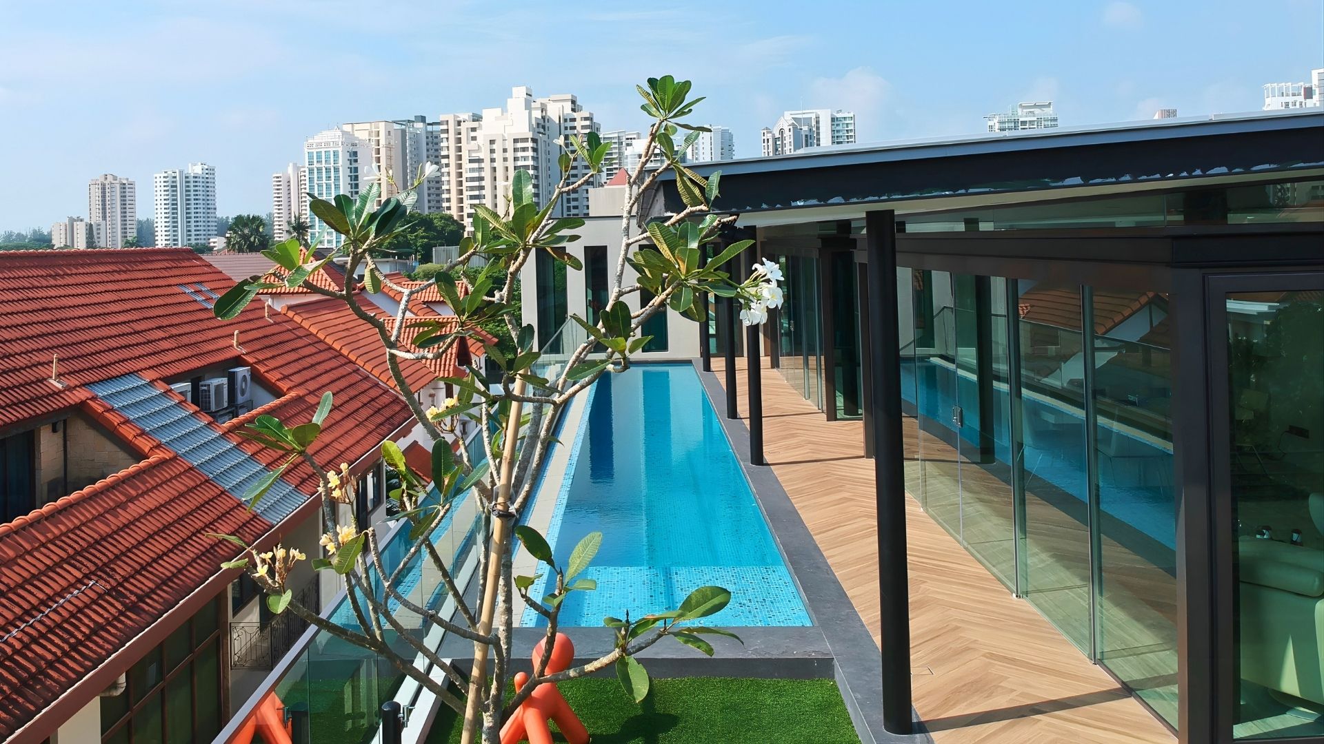 The well-manicured rooftop of a private landed home in Singapore. A lap pool made of stainless steel has been built next to the glass balcony, overlooking other houses to the left.