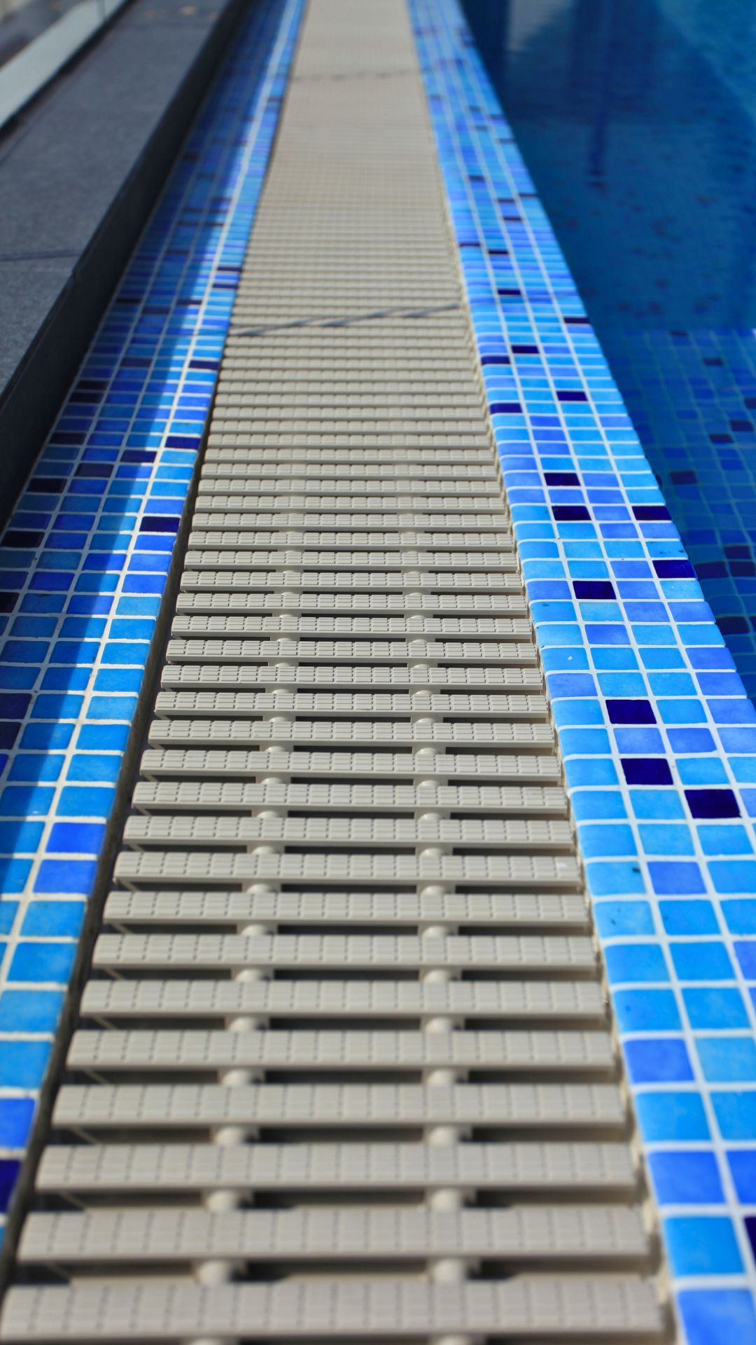 Close-up of the pool gutter at a private residence's swimming pool, which sits enclosed by blue and white mosaic tiles.