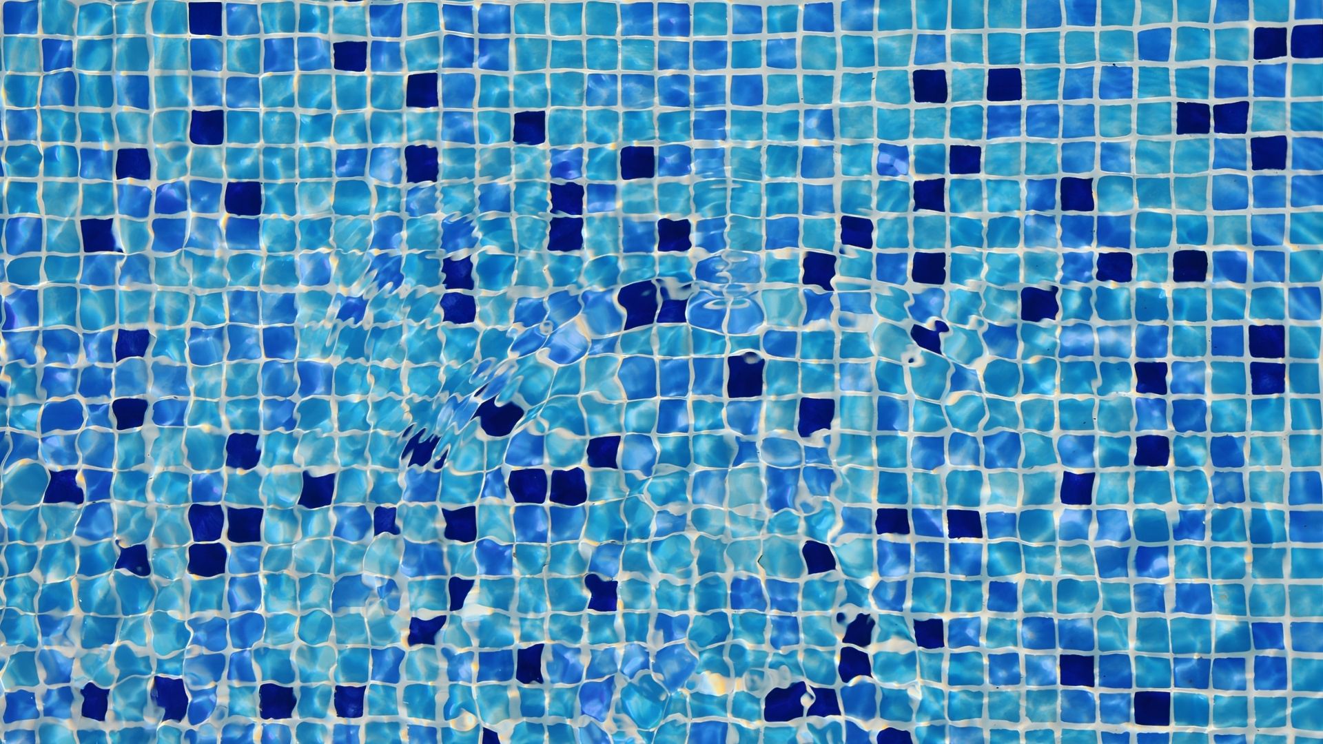 Close-up of the pool tiles at a private landed home in Singapore. The square tiles come in a mix of blue hues from sky-blue to indigo, divided by white borders.