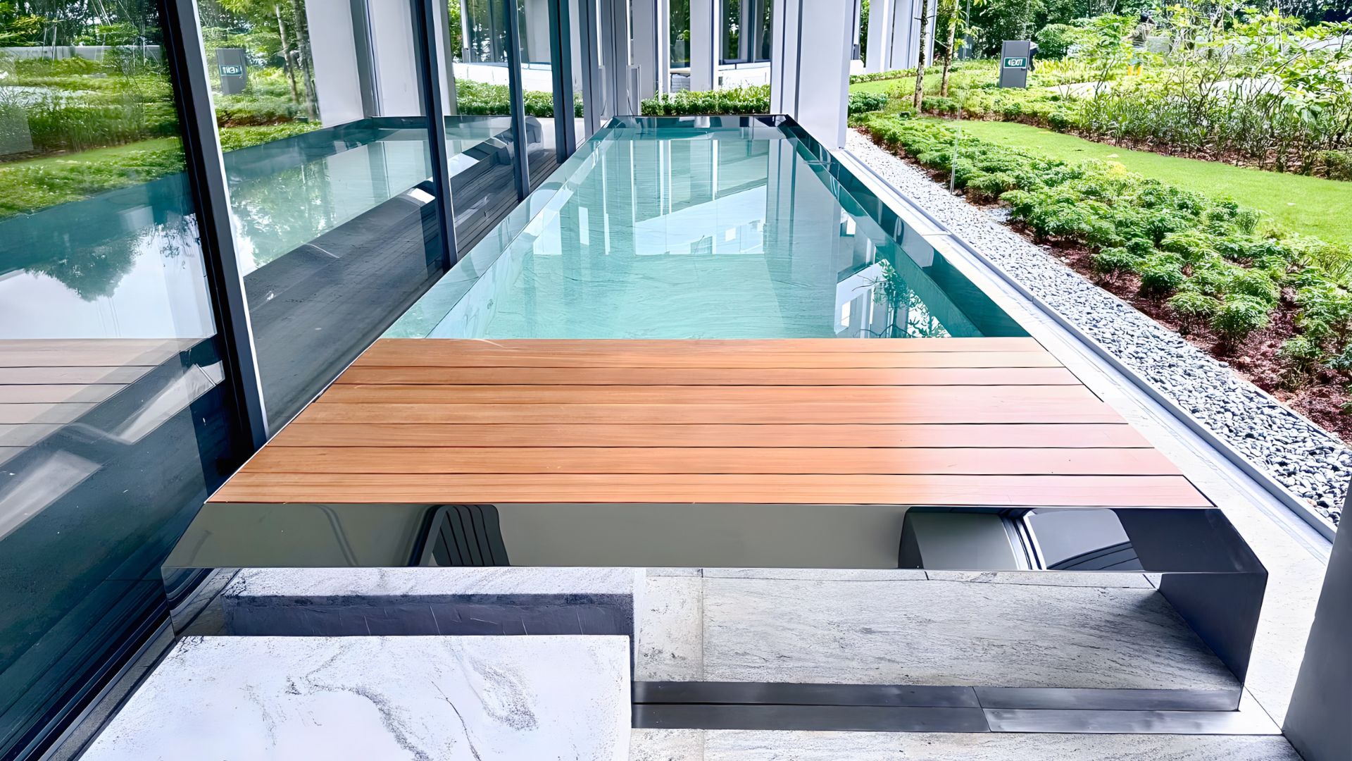 Exquisite stainless steel lap pool at Les Maisons Nassim in Singapore. A marbled stepping block to the side allows swimmers to step onto the wooden floorboards, before entering the pool. The surrounding landscape is lush with well-manicured greenery.