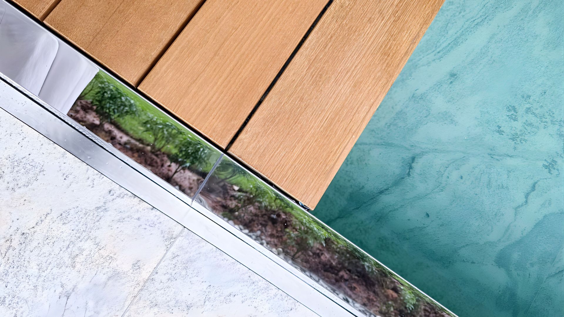 Diagonal close-up of a swimming pool at Les Maisons Nassim in Singapore. Wooden panels to the left lead into the pool, which is made up of fine viscount white granite. The pool looks out to verdant landscaped grounds.