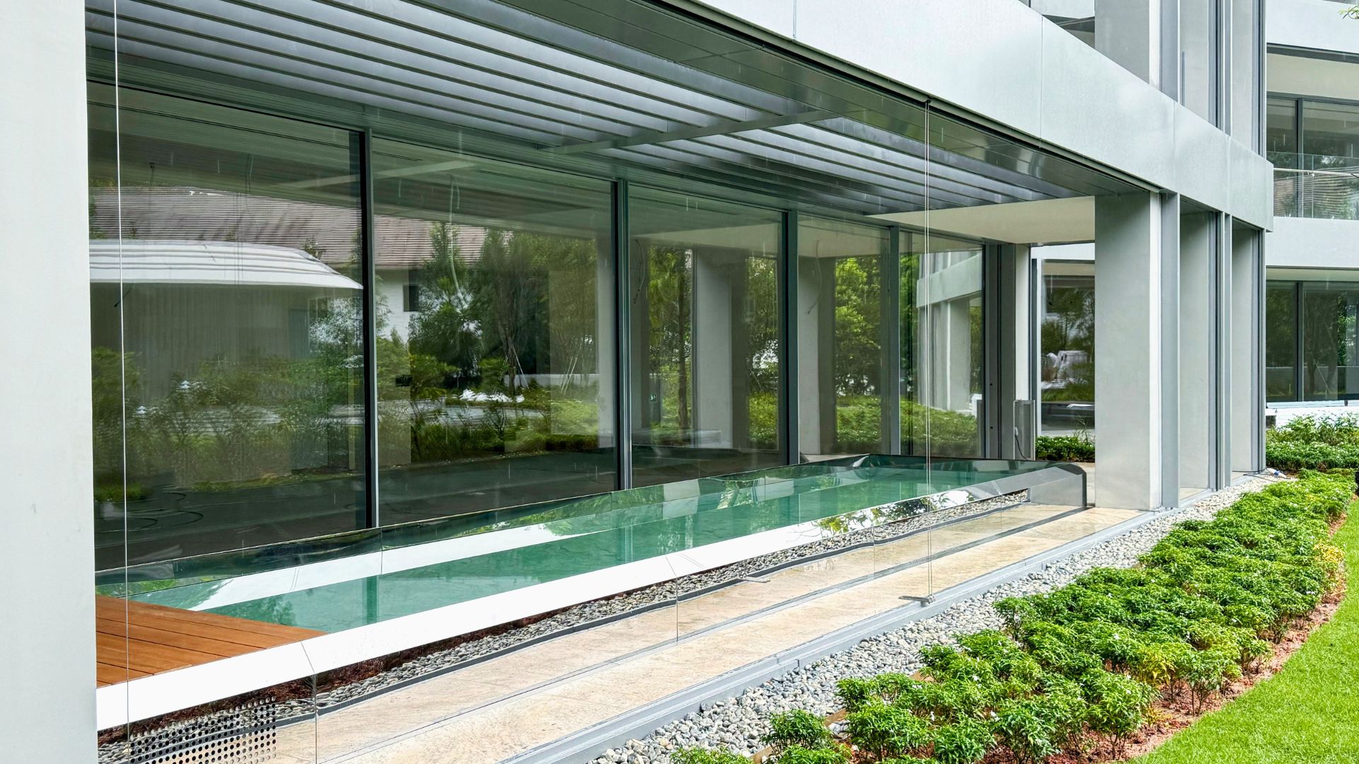 Stainless steel lap pool at Les Maisons Nassim in Singapore, cladded with mirror-finished stainless steel for a sleek architectural aesthetic. The mirrors at the edge of the pool reflect the sunlight, with a well-manicured lawn outside.