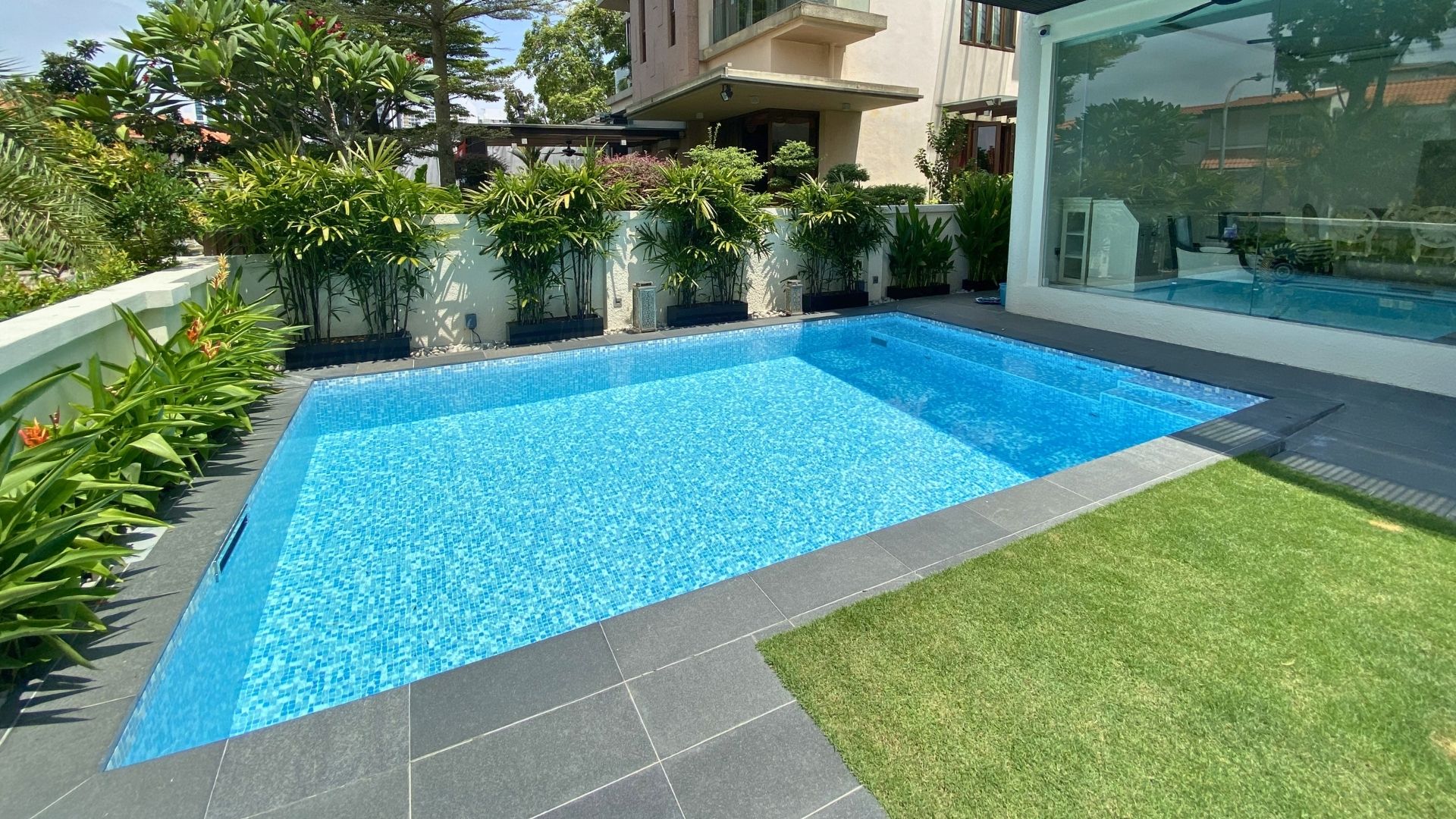 A private residential swimming pool pre-fabricated in stainless steel, and buried in-ground at the spacious front lawn of the house. The pool is overlaid with Spanish glass mosaic tiles, and surrounded by plants.