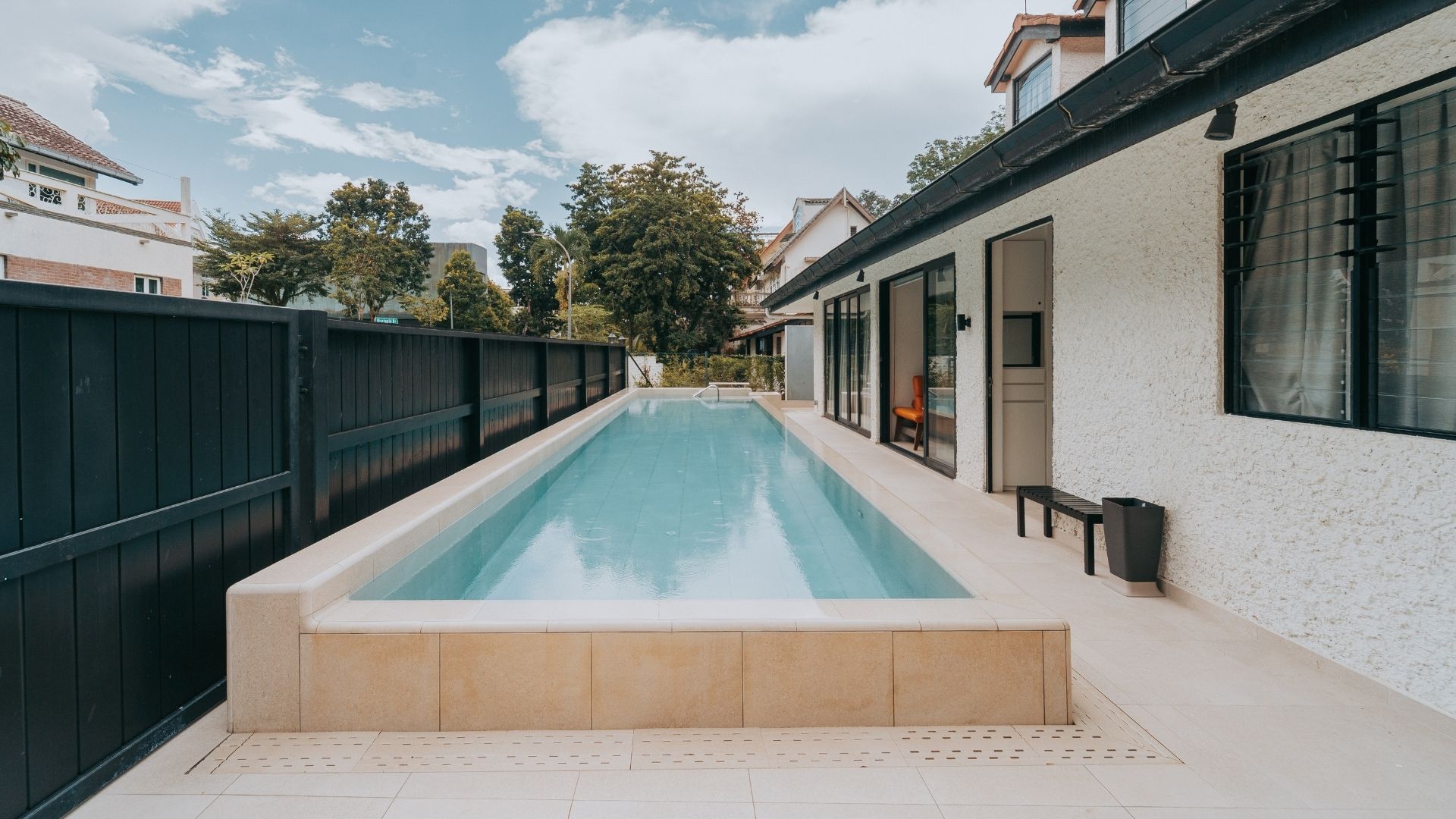 A newly-built 13.5 metre concrete swimming pool at the front porch of a private landed home in Singapore, finished with Spanish porcelain tiles in neutral tones to serve as a striking architectural feature that matches the house and its surroundings.