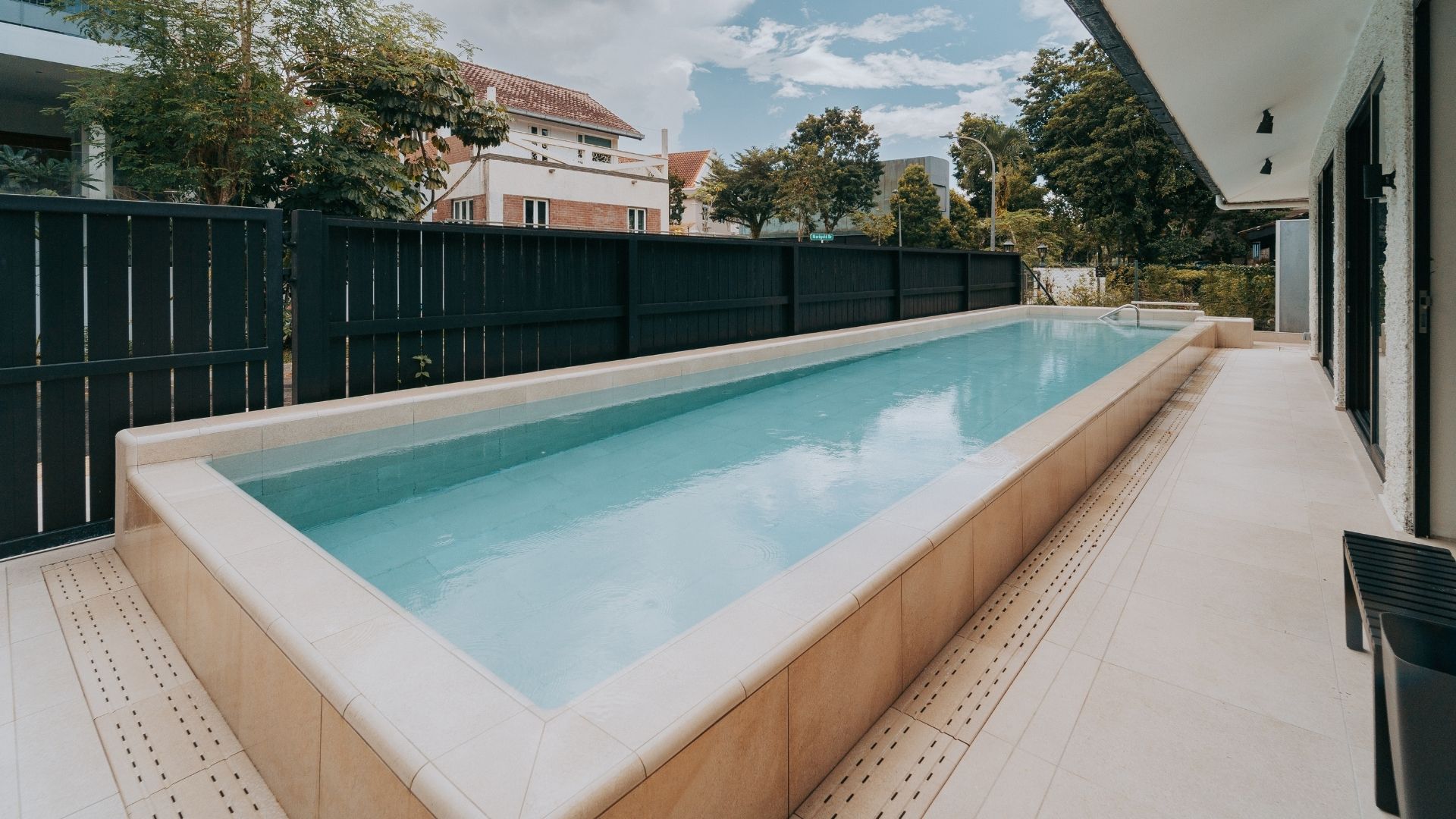 Diagonal view of a newly-buillt concrete lap pool at the front porch of a private residence in Singapore. It is made up of Spanish porcelain tiles in neutral tones for a sleek and elegant finish.