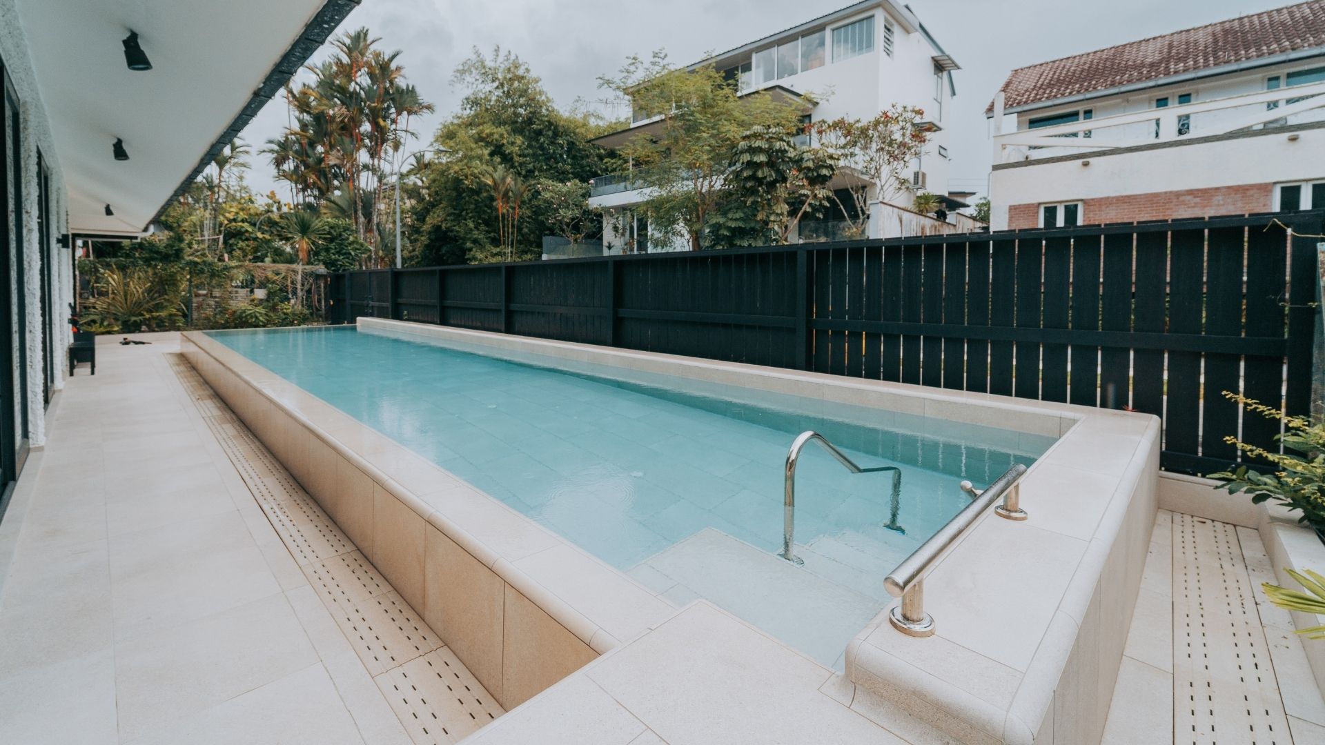 Grab rails allow for easy entry into the concrete lap pool at a private residence Singapore. The pool has been constructed in the front porch of the house, with wooden fences for privacy.