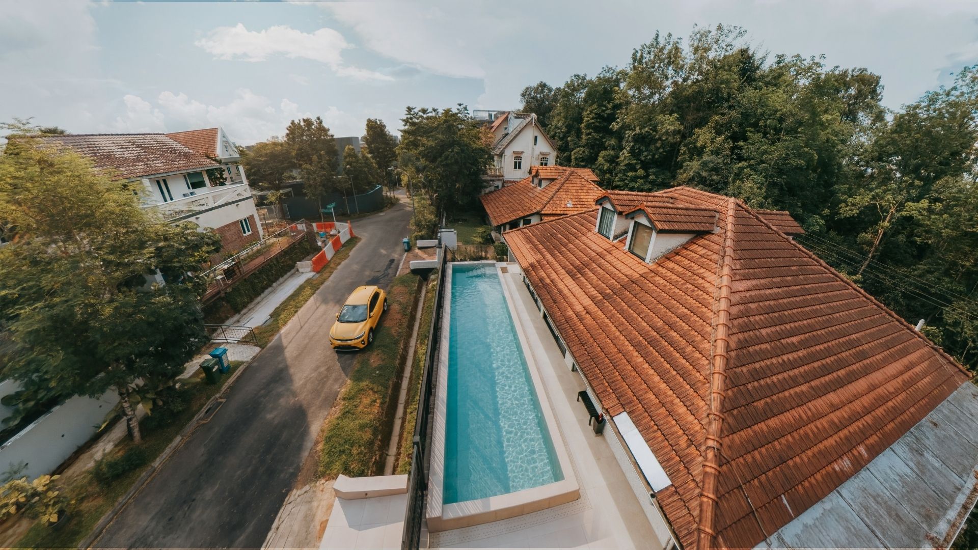 Full overhead view of a private landed home in Singapore. An off-white concrete swimming pool sits between the house and street, with a wooden fence enclosing it.
