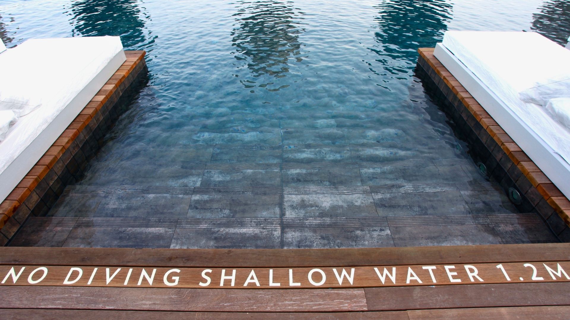 The instructions “no diving in shallow water 1.2 metres” are printed in white capital letters before the steps leading into the swimming pool at Marina Bay Sands (MBS), Singapore.