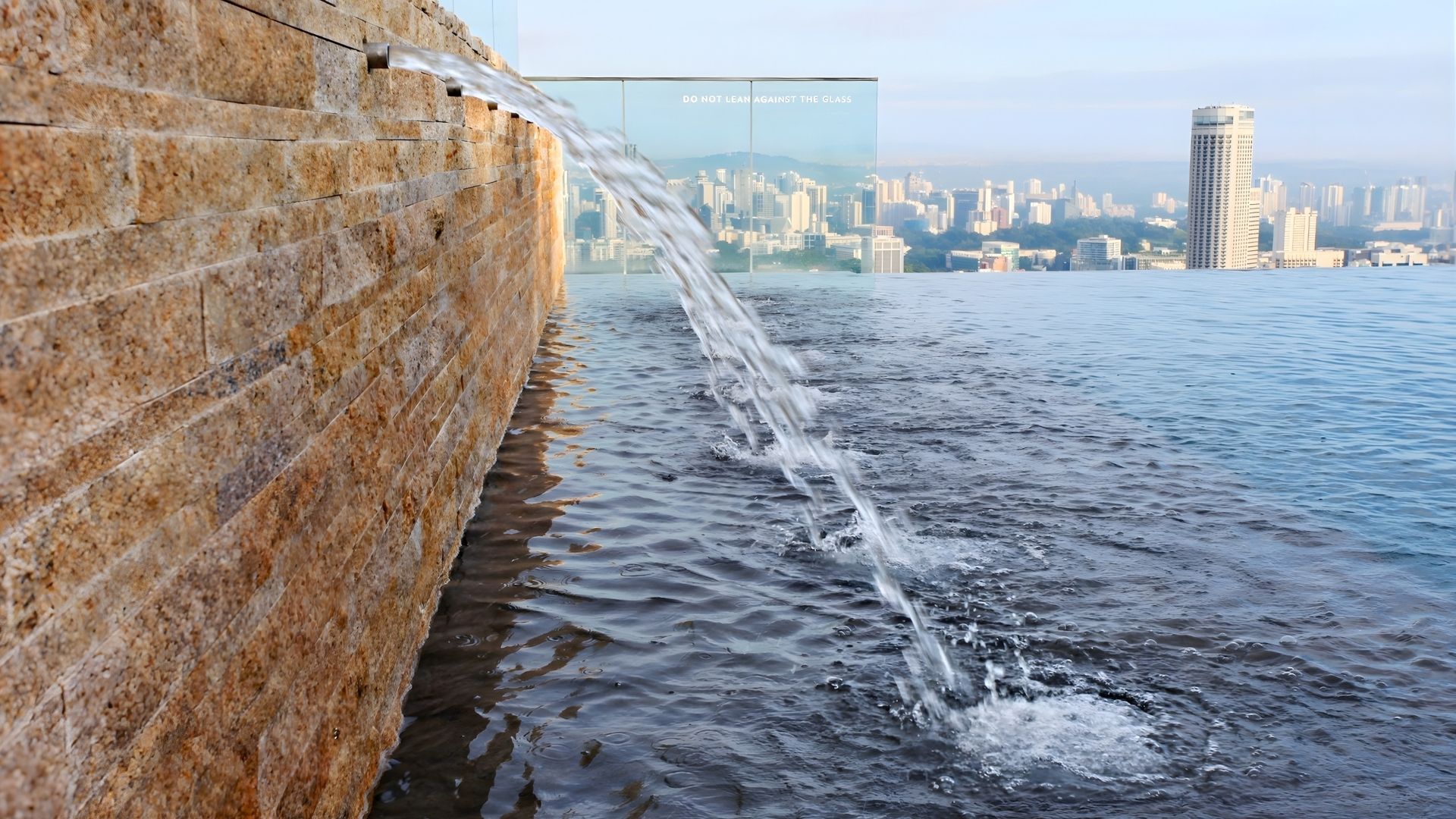 A water feature with water spouts lining a natural stone wall at one end of the Marina Bay Sands (MBS) SkyPark Infinity Pool.