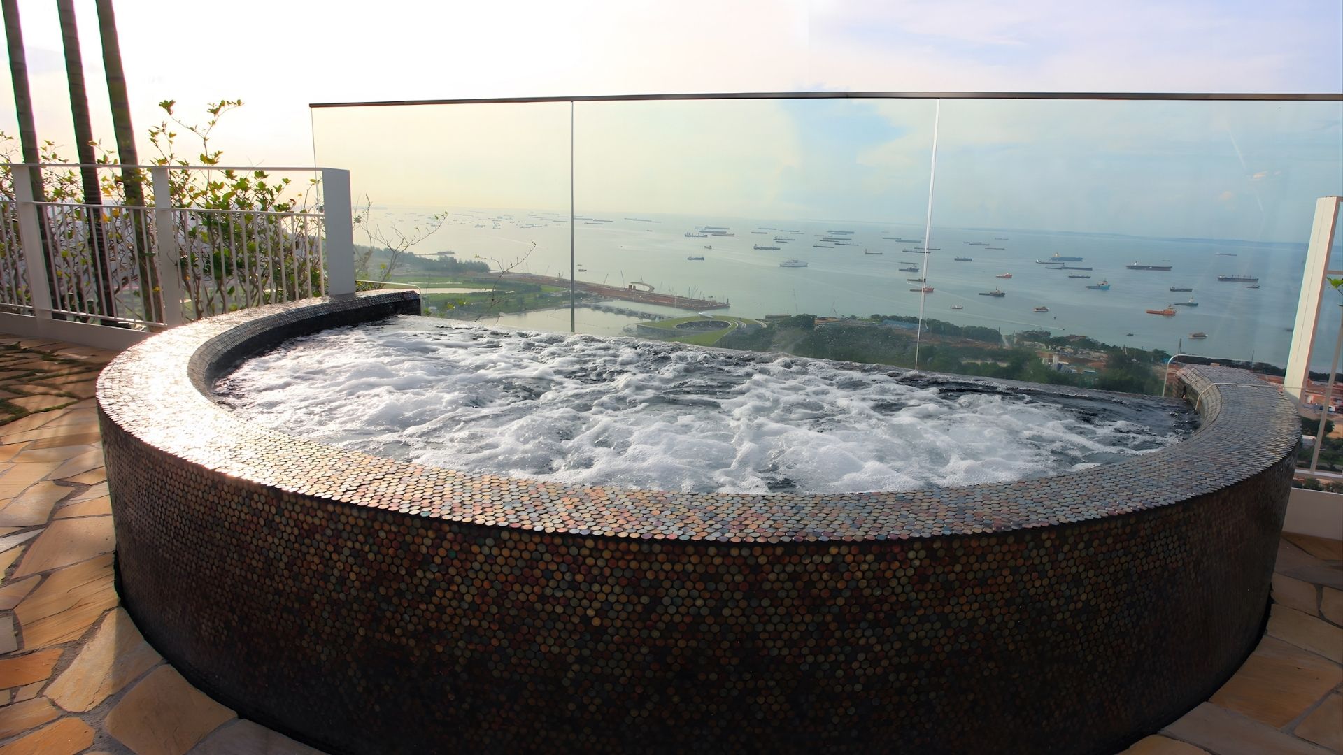 Bubbles cover the surface of the stainless steel spa tub at Marina Bay Sands in Singapore, as sunlight glints off the mosaic tiles at dawn or dusk. Ships ply along Marina Bay in the distance.