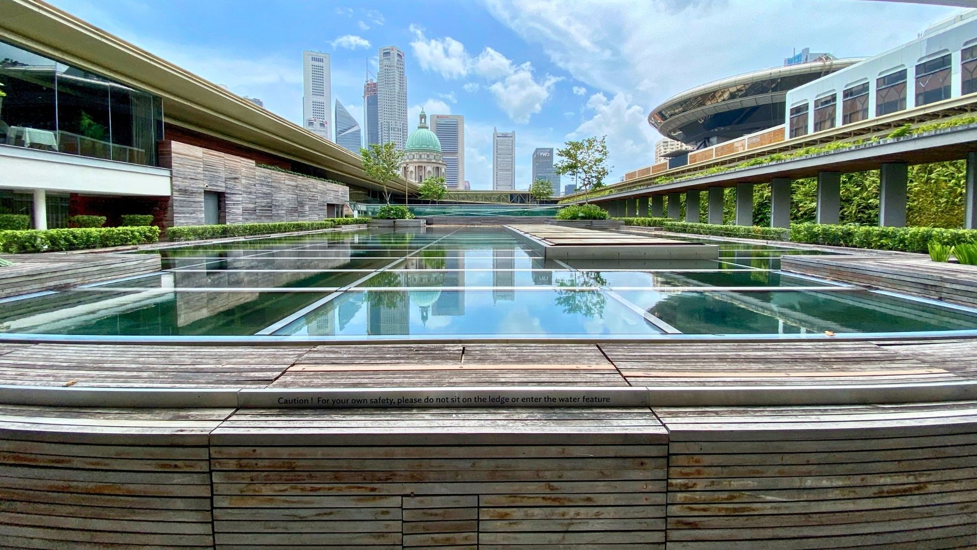 Eye-level view of the infinity-edge water features at the National Gallery Singapore, with tall skyscrapers in the distance.