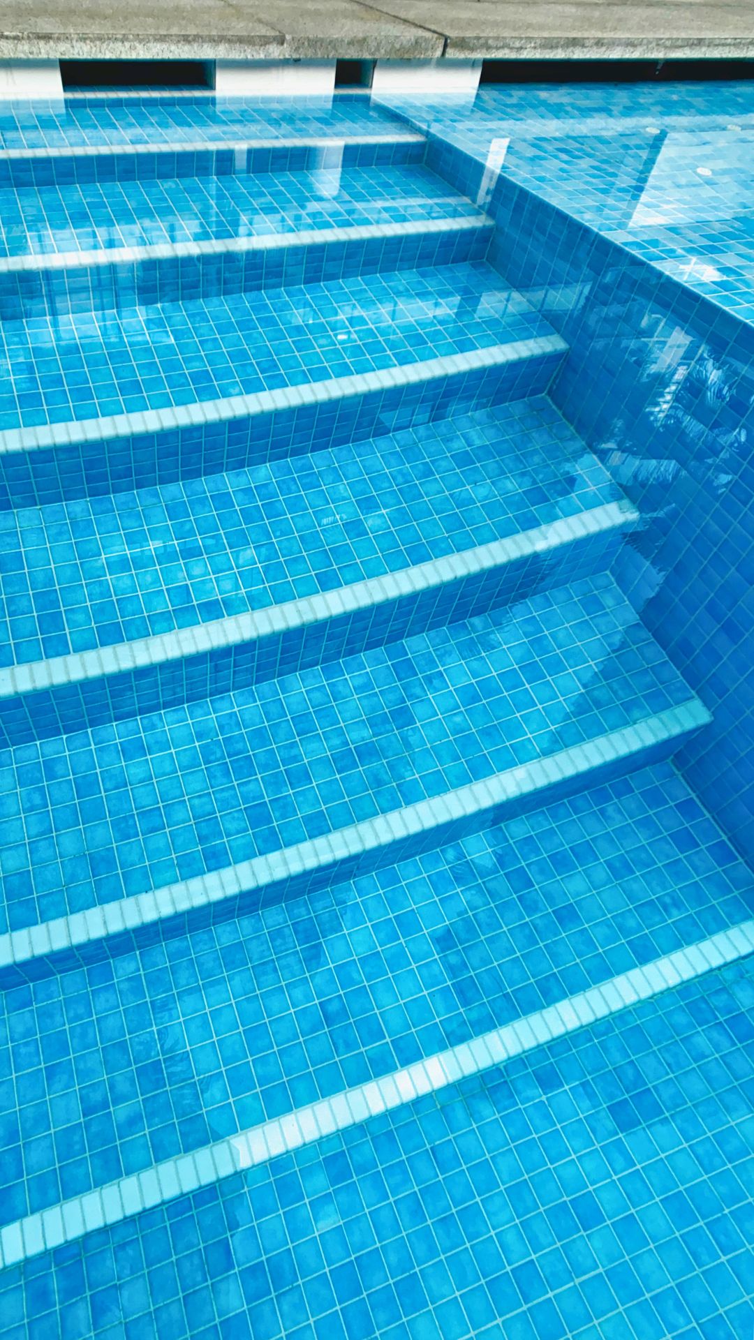 Close-up of the swimming pool steps at Paterson Suites condominium. The steps are finished in mosaic tiles, in bright and neat blue squares.