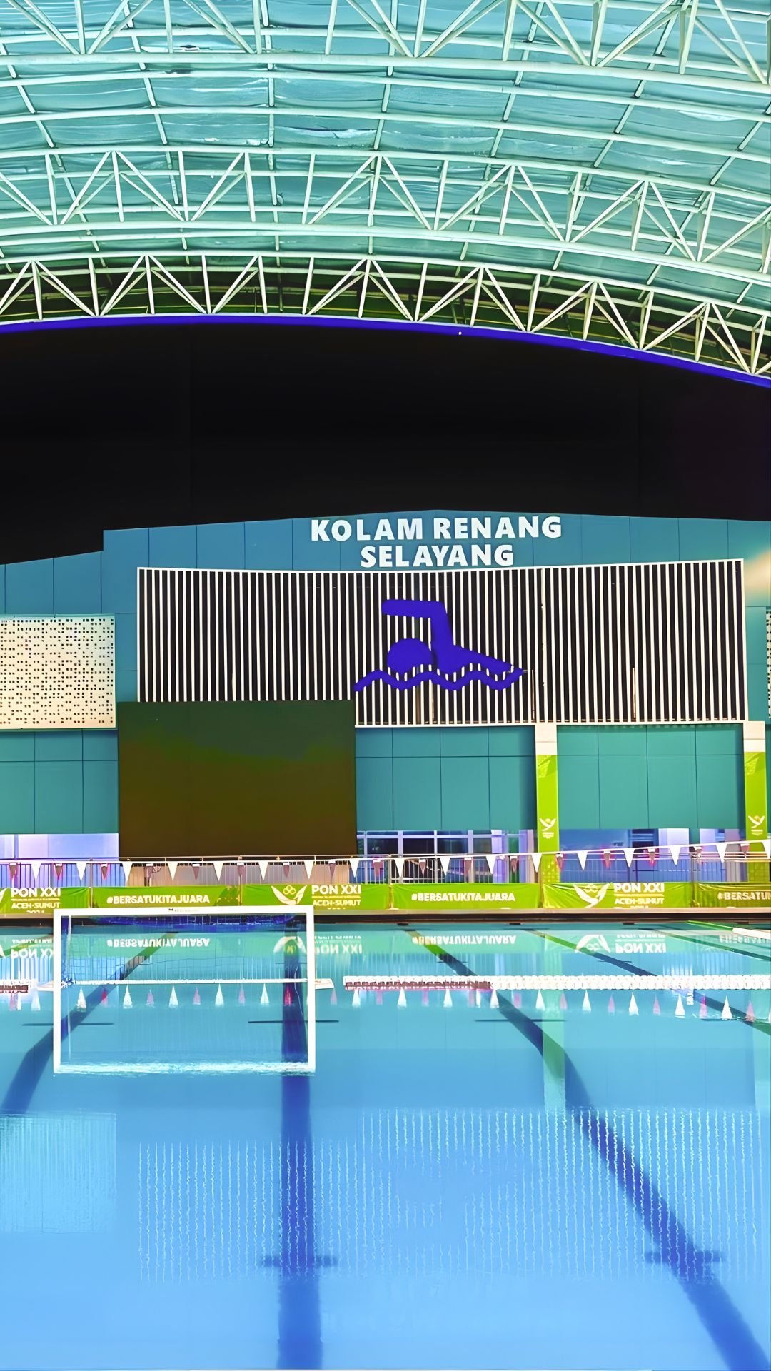 The words “Kolam Renang Selayang” are brightly lit up on a digital board, with a simple blue icon of a swimmer below it. A water polo net, pool flags, pool ropes, and other pool accessories are found within the competition pool.