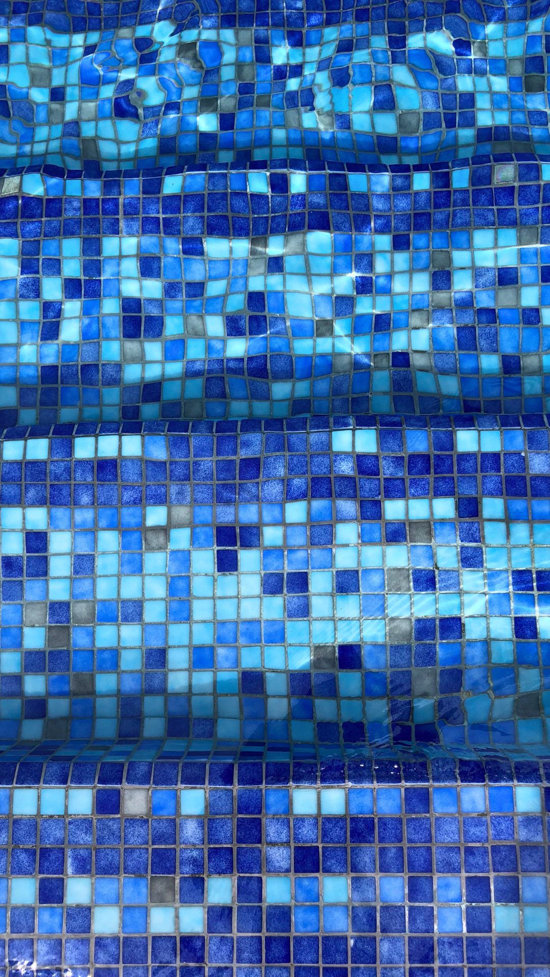 Close-up of the mosaic tiles of the spa pool, dancing beneath the water surface in mutiple shades of blue and azure at Our Tampines Hub, Singapore.