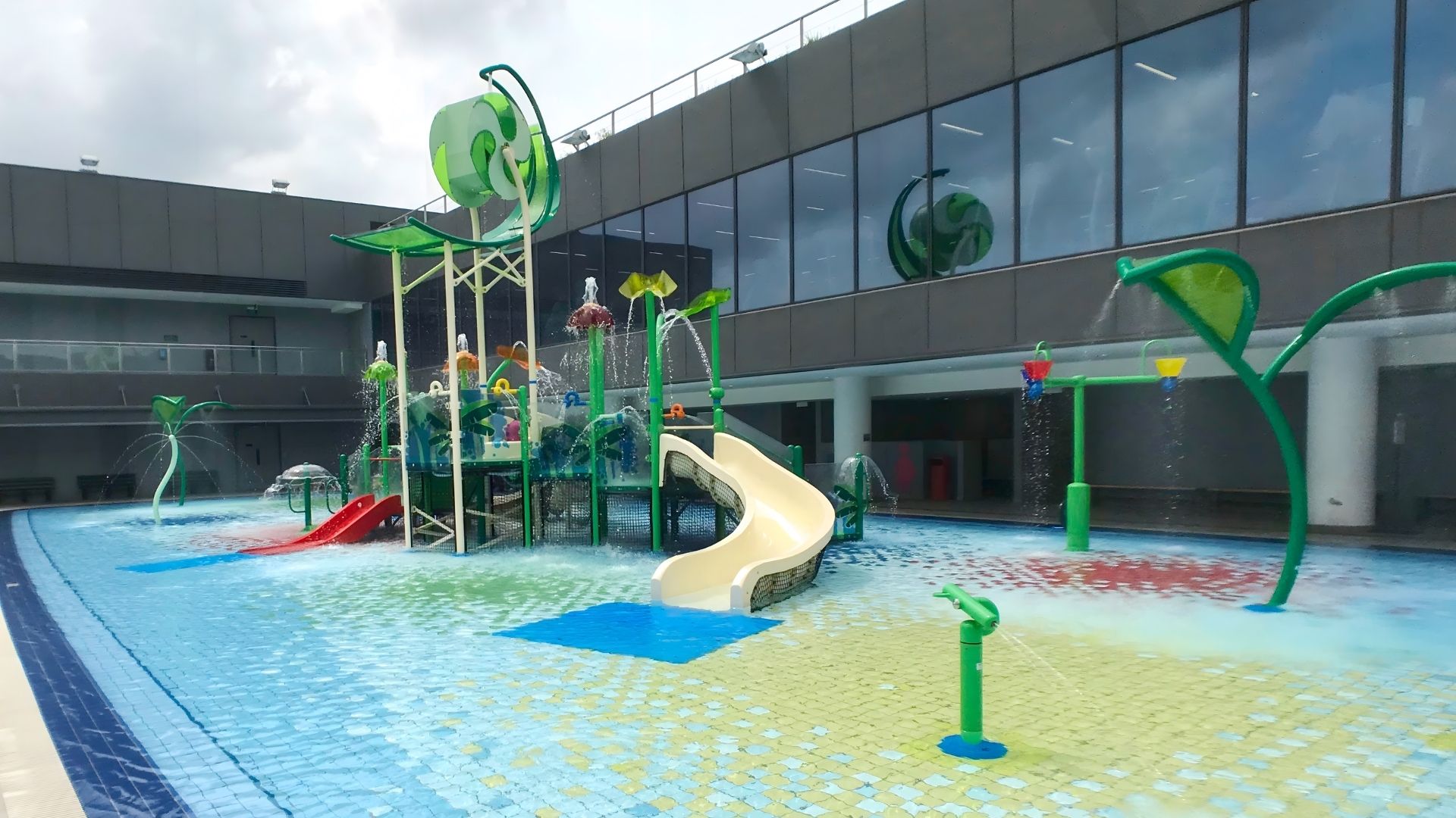 The wet playground for children at Our Tampines Hub in Singapore, complete with various brightly-coloured slides, connectors, and fun water play features that splash water out.