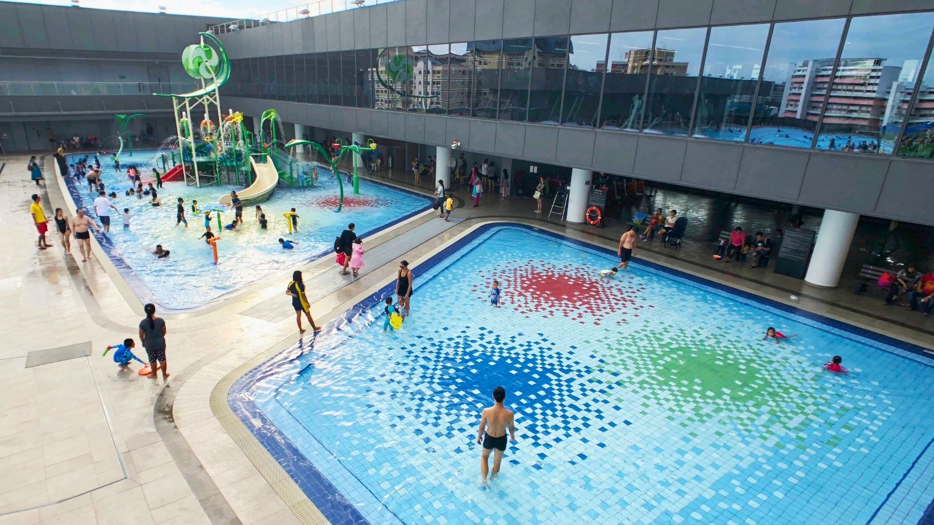 Top-down view of the wet playground and wading pool for kids at Our Tampines Hub in Singapore. Families occupy the facilities, playing with their children in the waters.