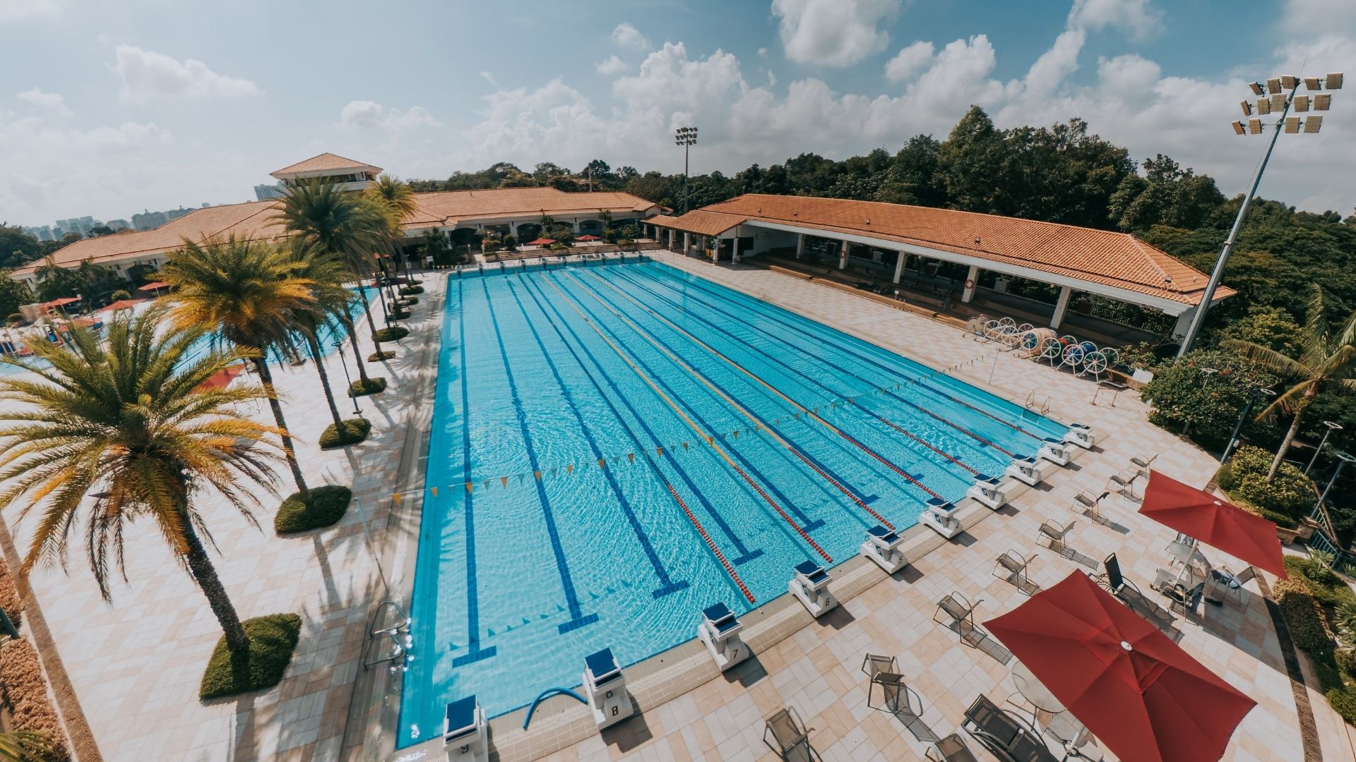 Overhead view of the 50-metre competition swimming pool at the Singapore Island Country Club, which looks renovated. The pool contains all essential pool equipment and accessories. The sitting areas around the pool deck are well-sheltered by umbrellas.