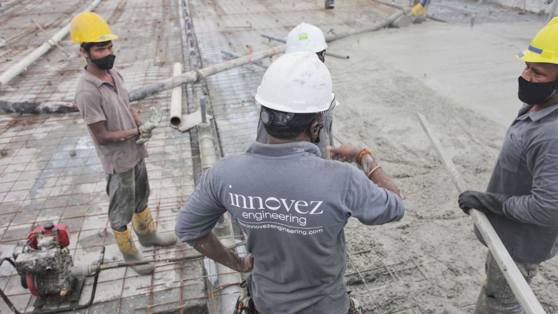 Construction workers from Innovez Engineering dressed in protective gear are discussing the work plan. The concrete casting of the pool floor is underway at the Singapore Island Country Club, with metal rebar structures still uncovered in many areas.